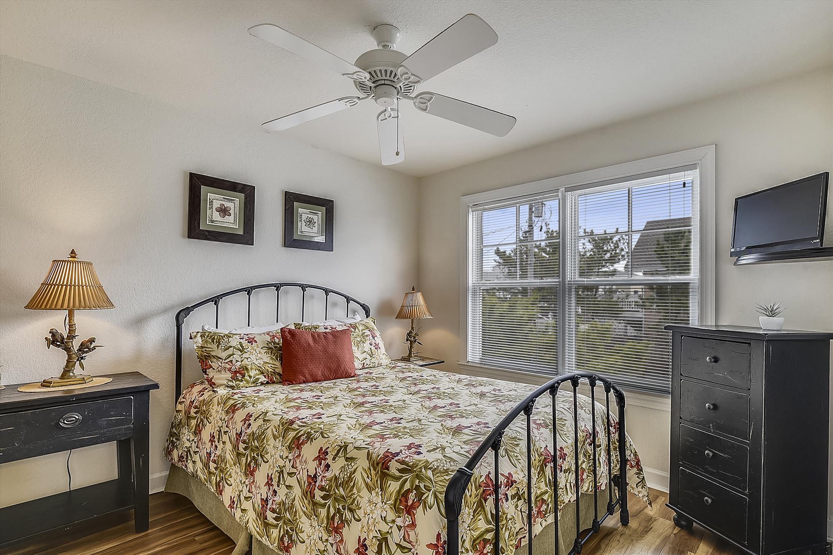 Unwind in your cozy retreat featuring a plush bed dressed in cheerful florals, warm bedside lamps, and a mounted TV for your favorite shows.