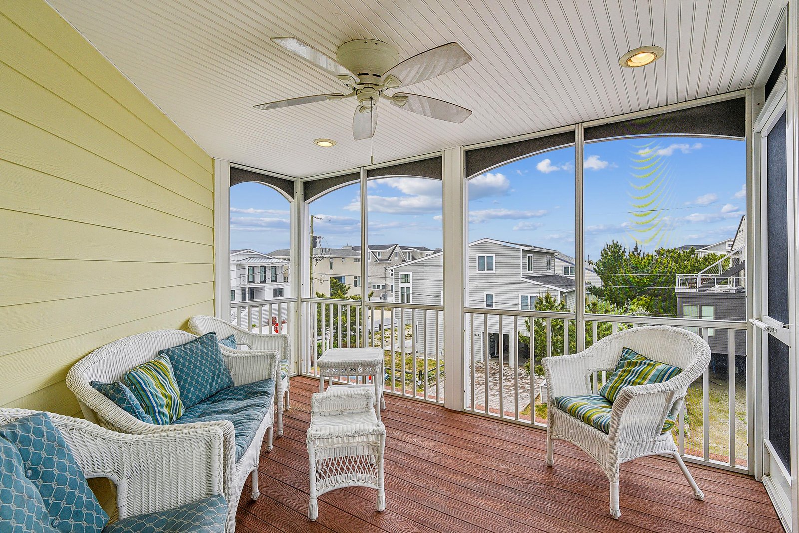 Relax on your screened-in porch with comfortable wicker seating, a ceiling fan overhead, and peaceful neighborhood views through the windows.
