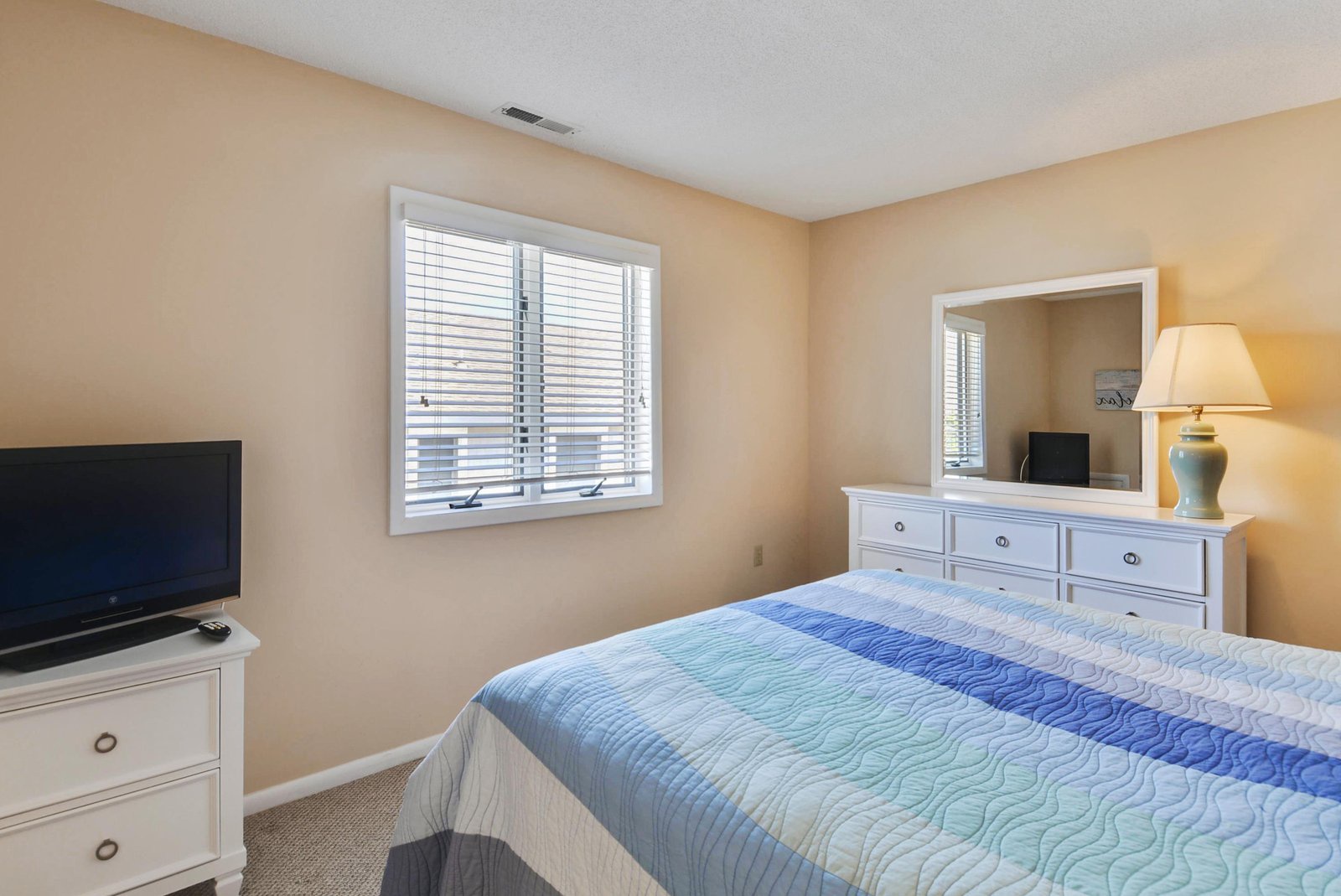 Your peaceful retreat features a cozy queen bed with coastal-inspired linens, a dresser with mirror, and your own flatscreen TV for unwinding after a day of exploring.