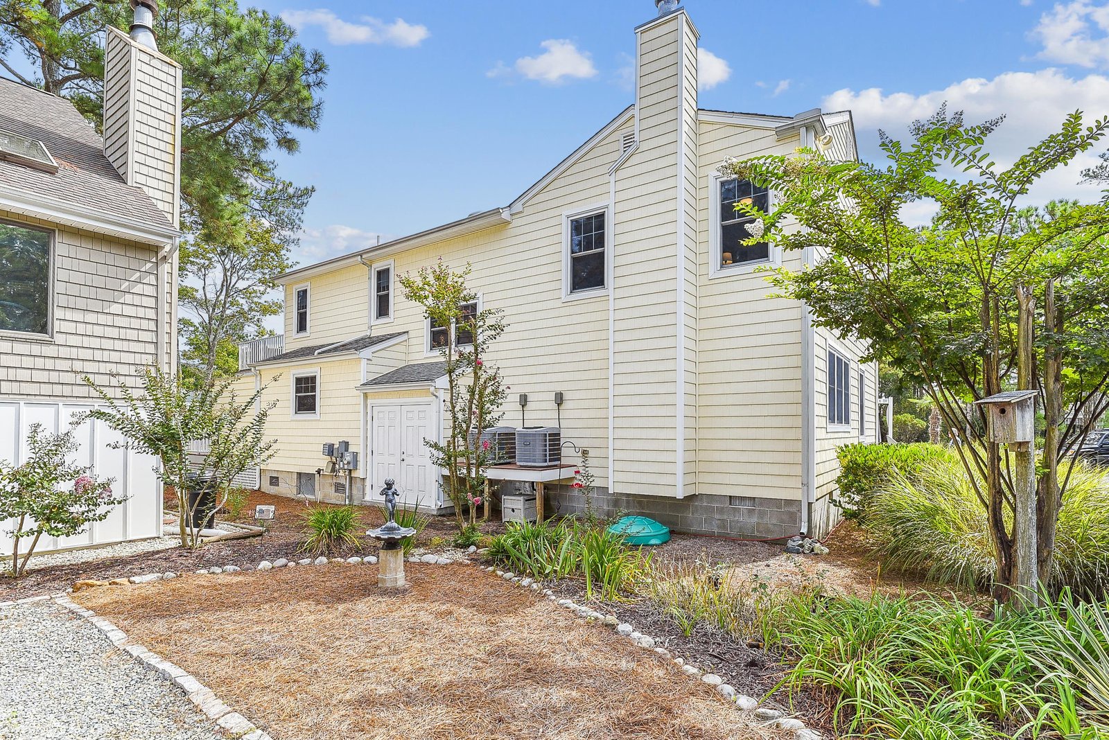 A bright two-story home nestled among mature trees and native coastal landscaping under a beautiful Carolina sky.