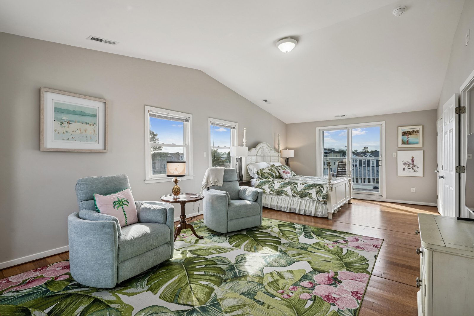 Wake to soft natural light streaming through windows, perfect for your coastal escape. This spacious bedroom blends relaxation with tropical elegance—plush seating, gleaming hardwood, and cheerful décor make mornings feel like paradise.