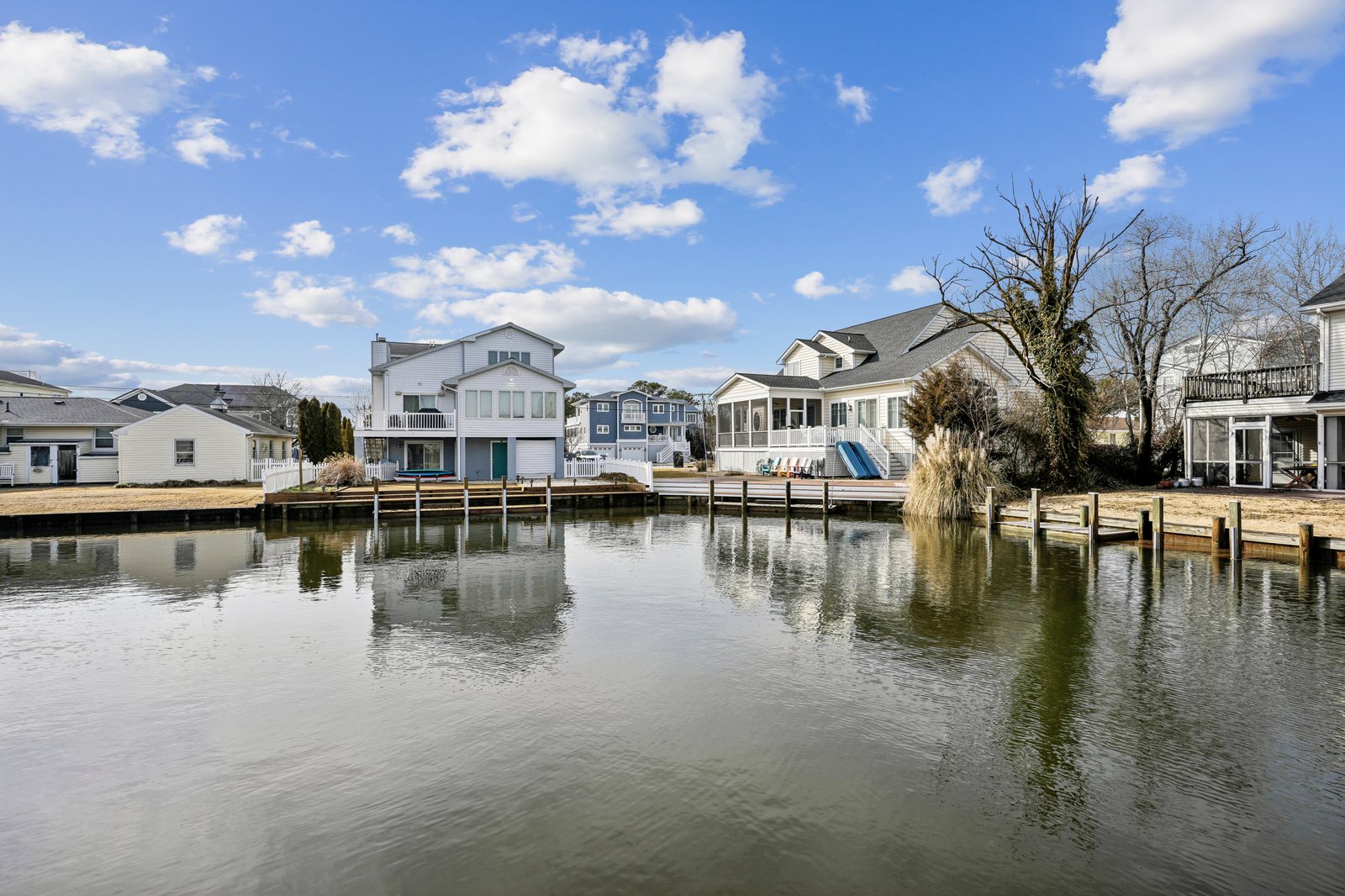 Waterfront homes line a peaceful canal with private docks under a bright blue sky with fluffy white clouds.