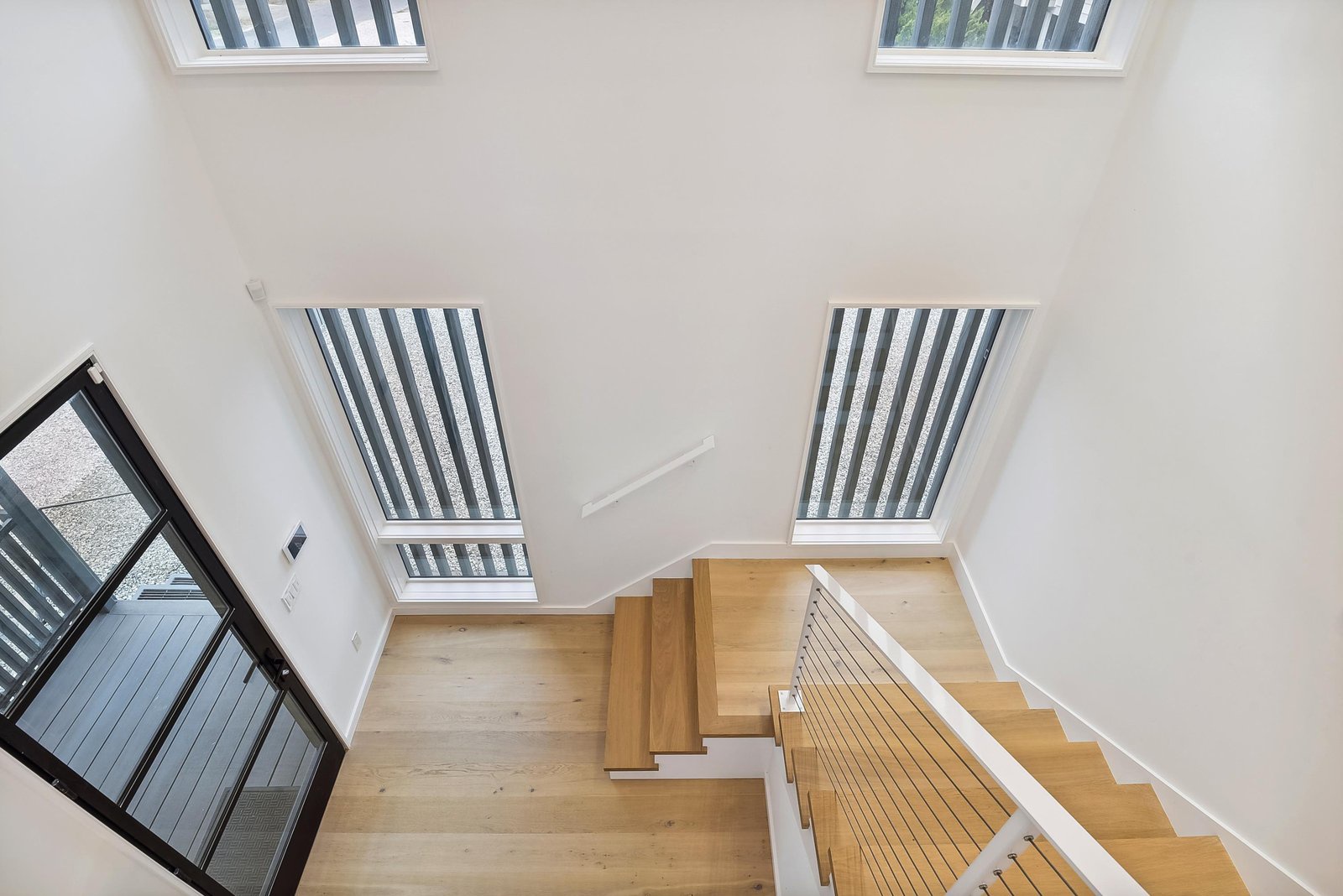 Sunlight streams through sleek skylights, illuminating the modern wooden staircase and creating a bright, airy atmosphere throughout the space.