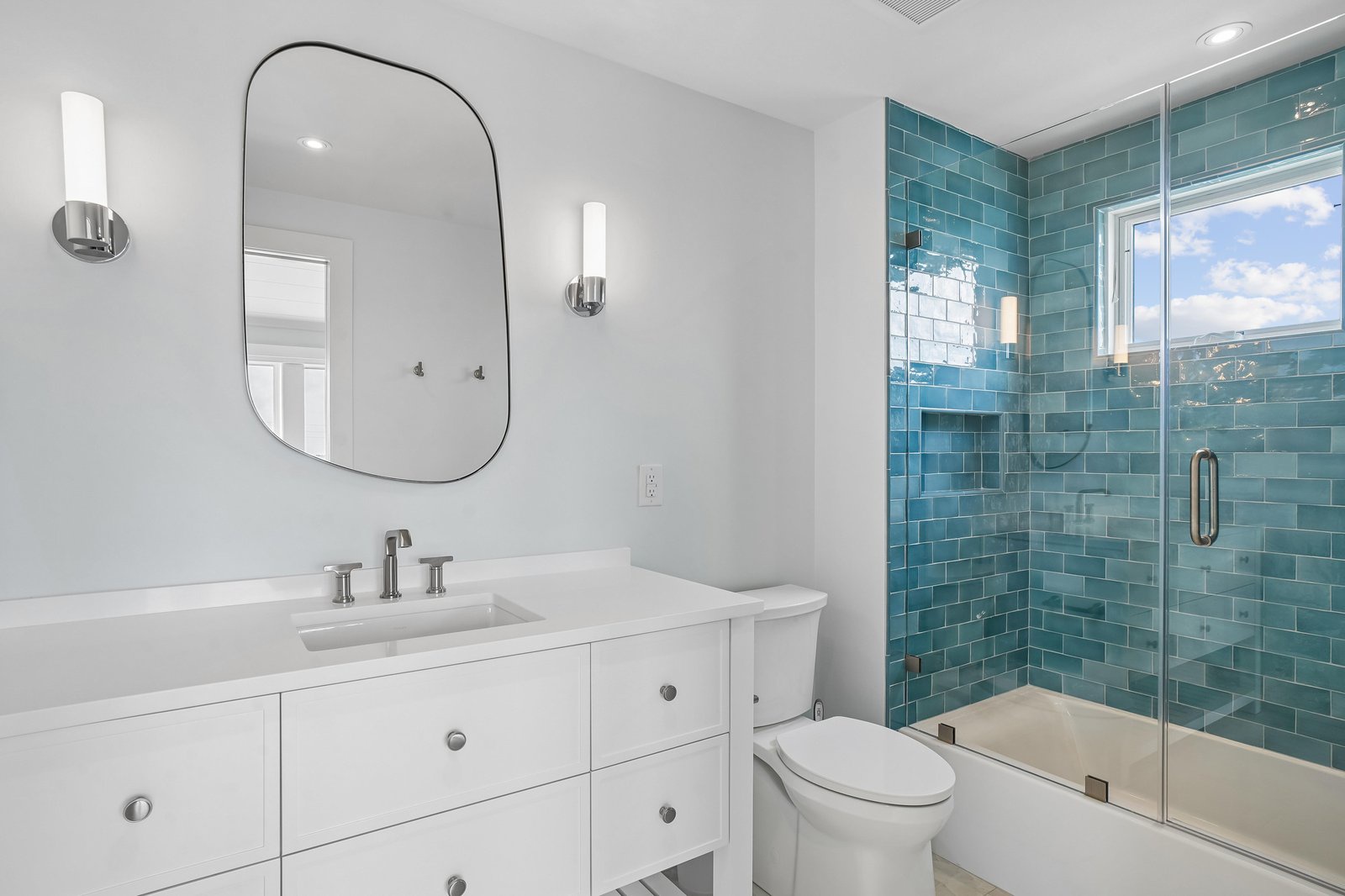 Refresh yourself in this modern bathroom with stunning turquoise tile, a sleek glass-enclosed tub, and warm natural light streaming through the window.