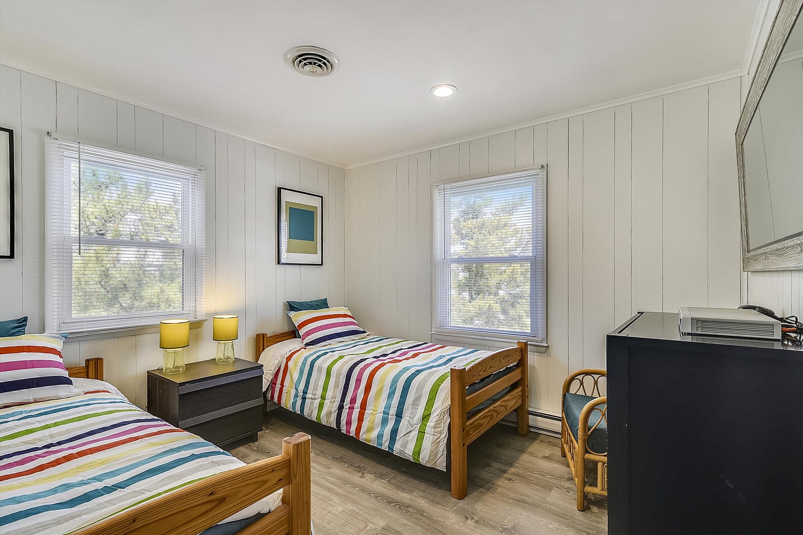 Bright twin bedroom with cheerful striped linens and natural light—perfect for kids or friends traveling together, with windows showcasing leafy views.