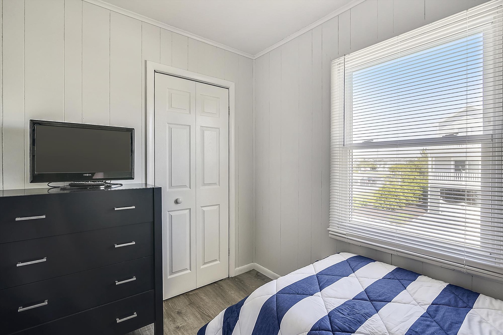 Your cozy bedroom features a comfortable bed, ample storage, and a flat-screen TV. Natural light streams through the window, creating a bright, welcoming space for restful nights.