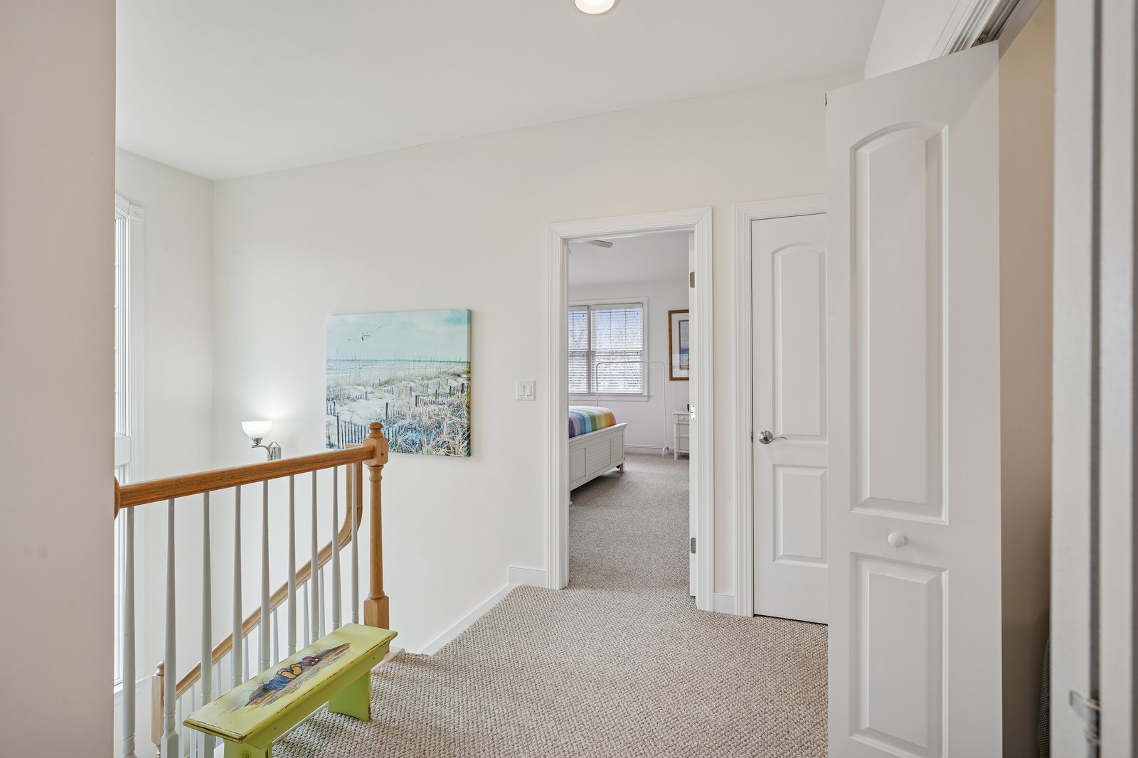 Step into your bright upstairs hallway where coastal artwork greets you and bedrooms await behind cheerful white doors.