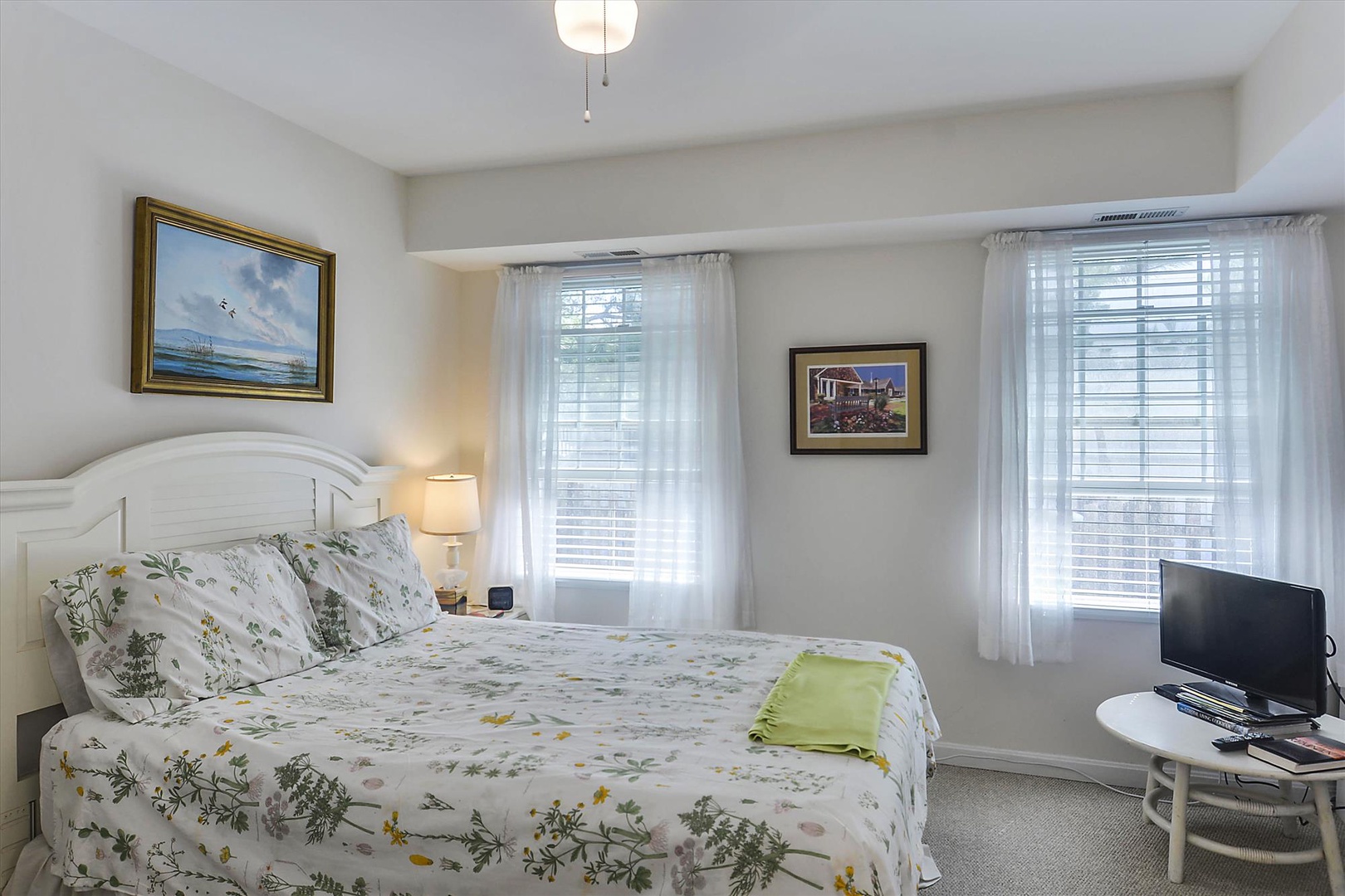 Soft natural light pours through dual windows in your peaceful bedroom retreat, where botanical linens and cheerful artwork create a bright, welcoming sanctuary for restful nights.