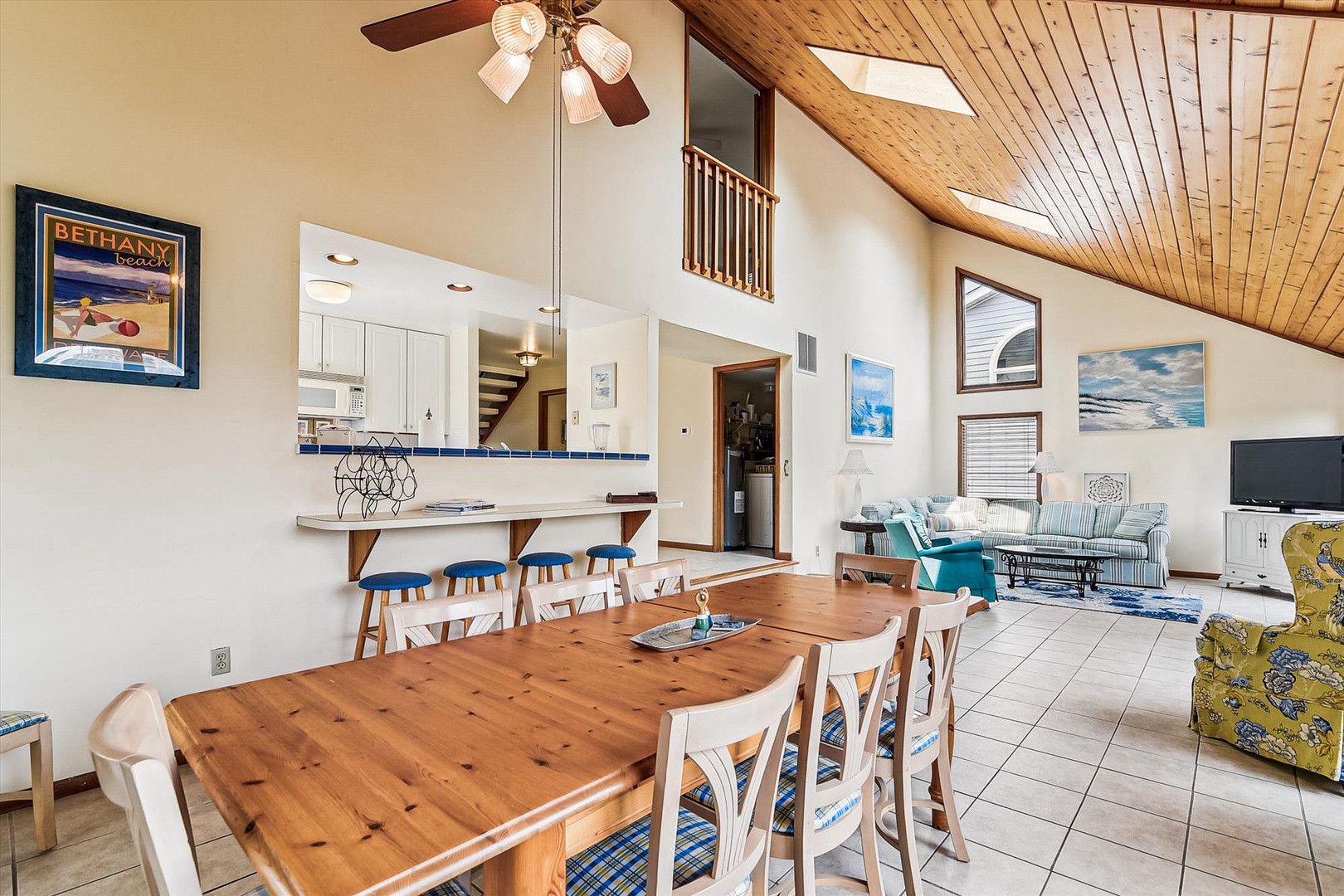 A bright, airy main living area where you'll gather around the handcrafted wood dining table, relax on colorful seating, and enjoy soaring ceilings that flood the space with natural light and coastal charm.