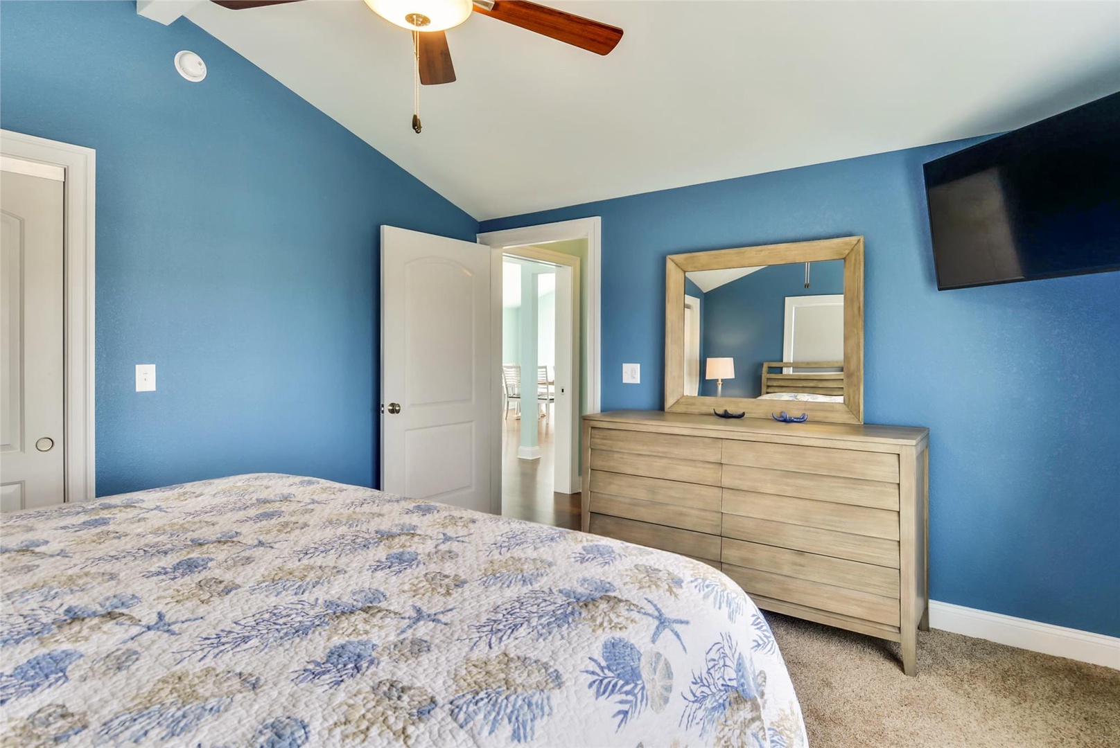 Rest easy in your serene bedroom with soothing blue walls, a plush bed dressed in coastal linens, and modern comforts like a ceiling fan and flat-screen TV.