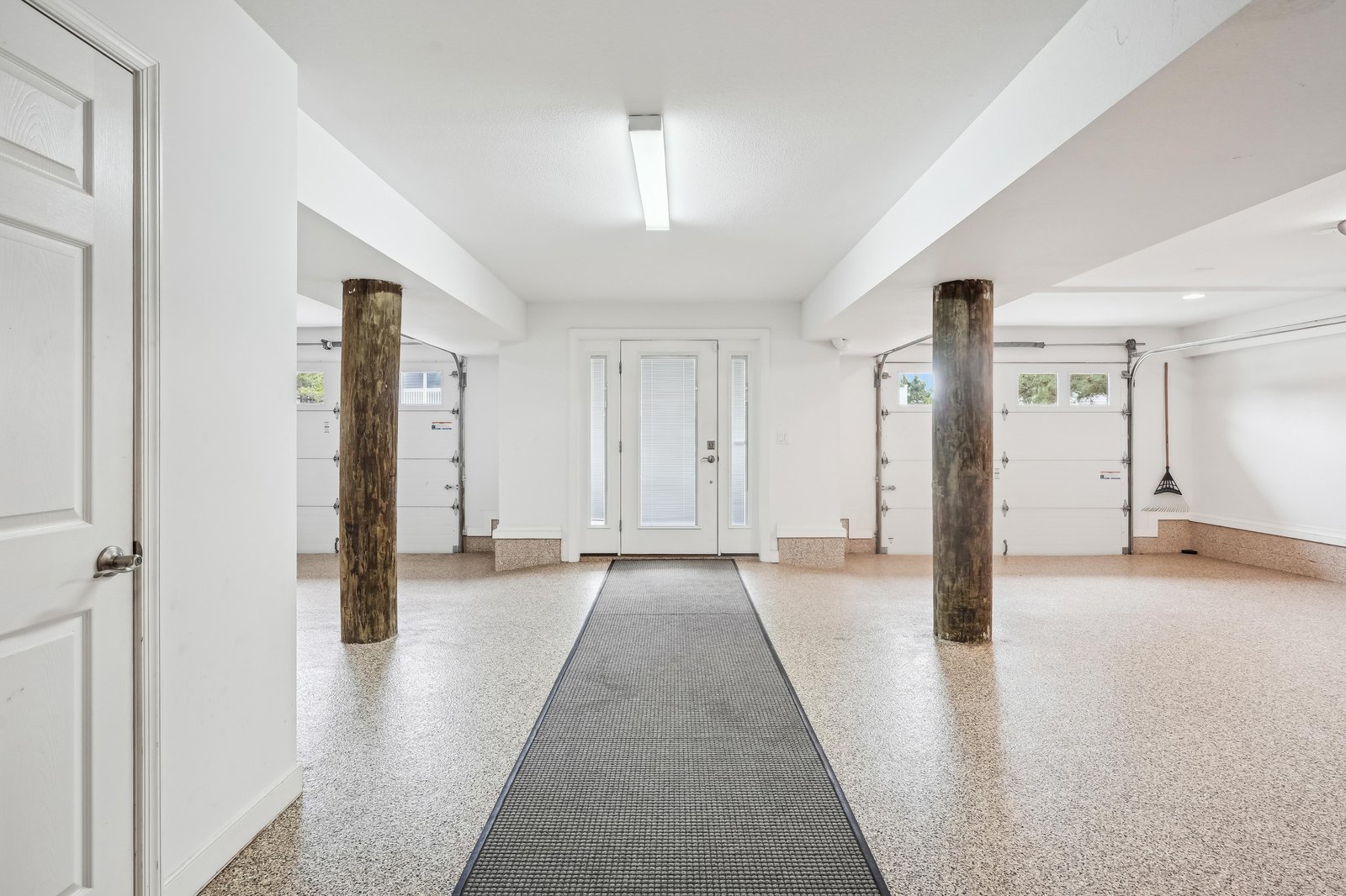 The property features a spacious finished garage with distinctive rustic log beam accents, bright white walls, and durable epoxy flooring—offering flexible space for parking, storage, or recreation.