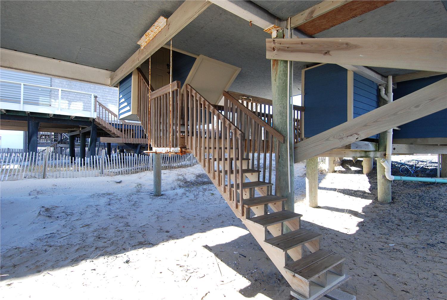 A beachfront property elevated on sturdy pilings, offering covered parking and ground-level storage beneath. Sandy pathways and coastal architecture invite a classic beach escape.