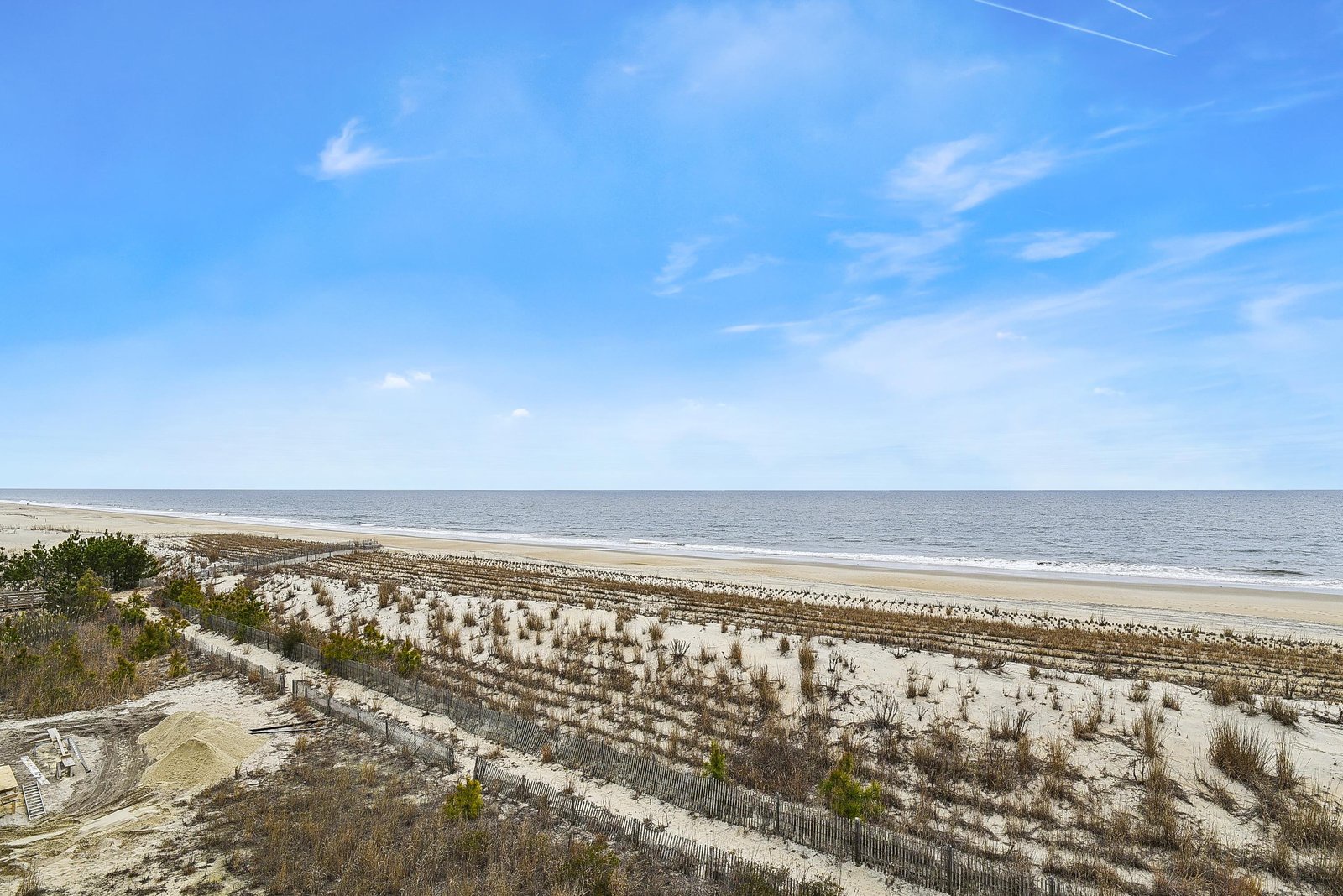 A pristine stretch of sandy shoreline awaits, framed by rolling dunes and the endless expanse of ocean meeting a brilliant blue sky—perfect for morning strolls or sunset watching.