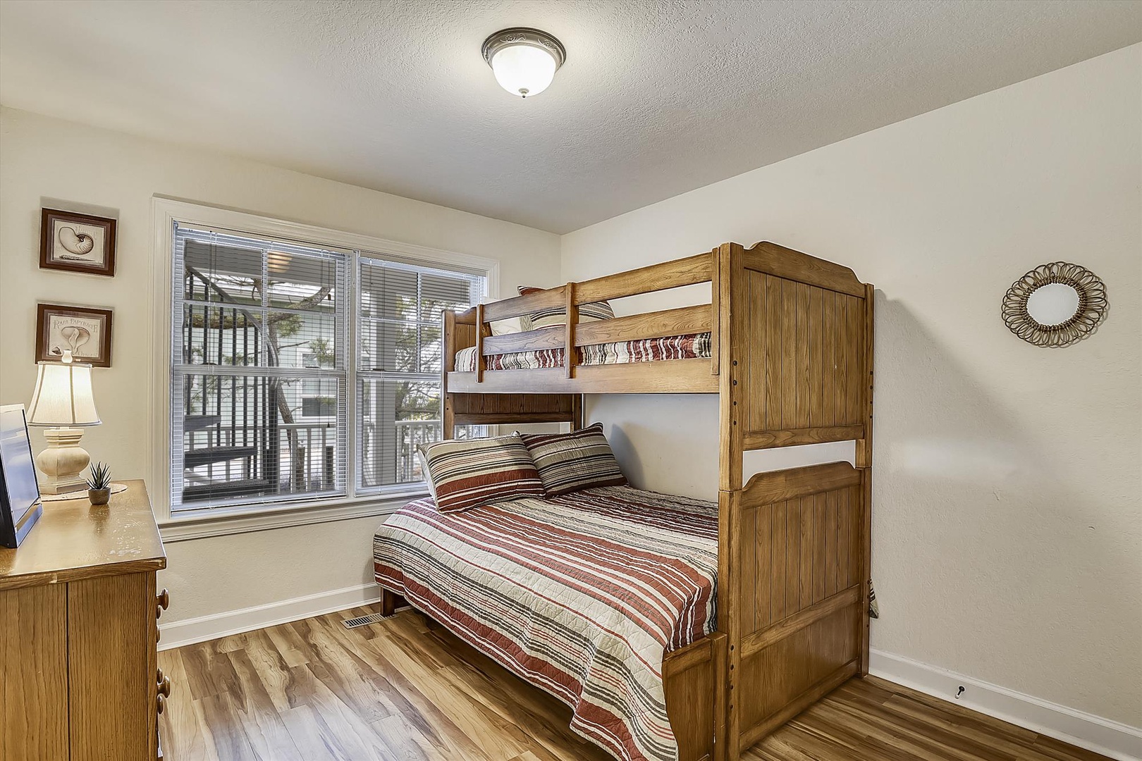 Your cozy bedroom features a sturdy wooden bunk bed with comfortable striped bedding, perfect for kids or extra guests. Natural light filters through the window, and warm wood floors add a welcoming touch.