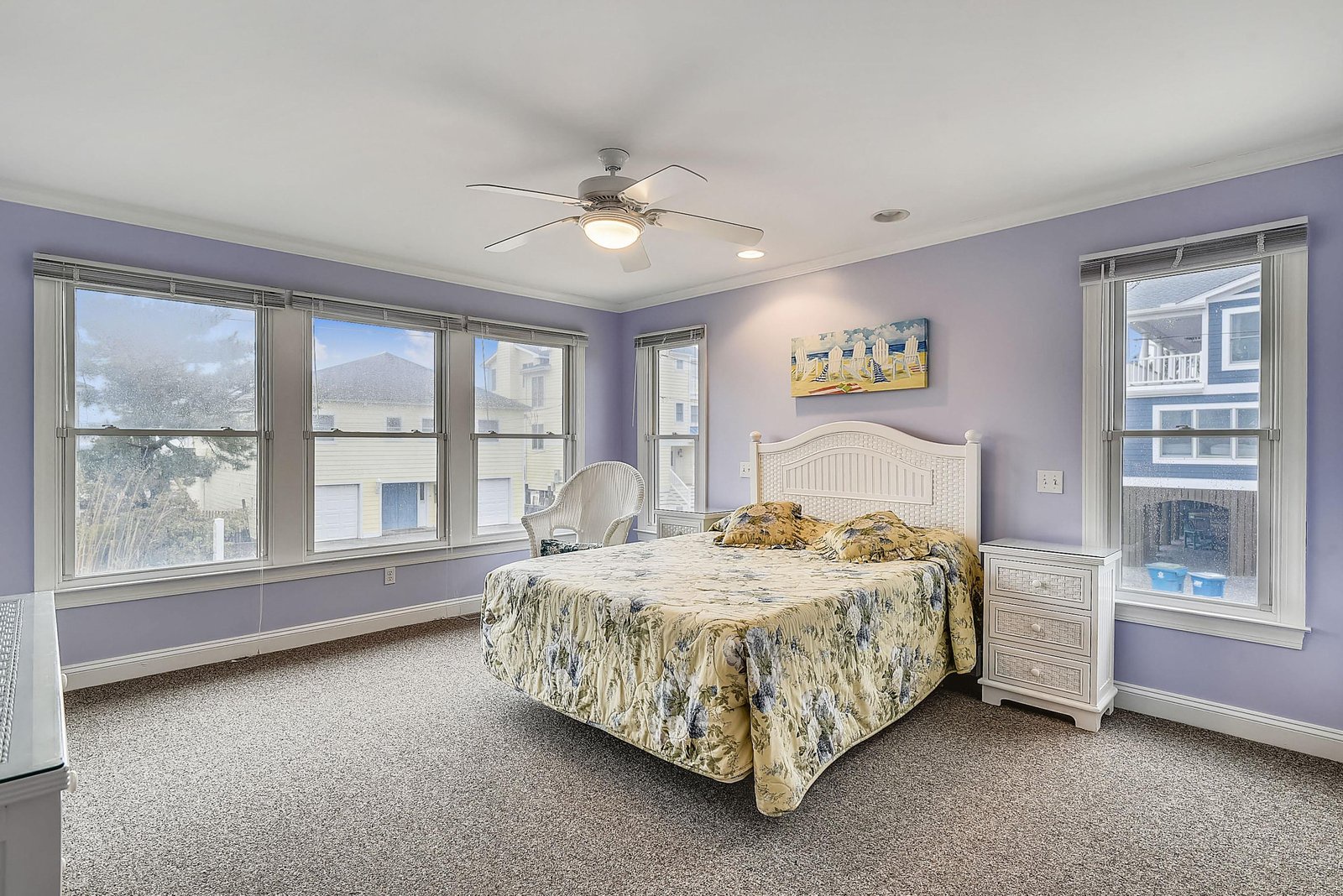 Your peaceful retreat features a plush queen bed, calming lavender walls, and plenty of natural light from windows on three sides. The ceiling fan keeps you comfortable while you unwind in your own private haven.