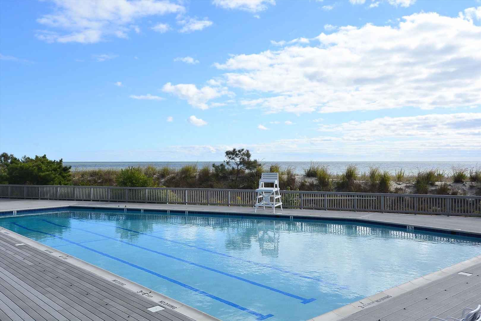 Beachfront pool area with crystal-clear waters and ocean views beyond the dunes.