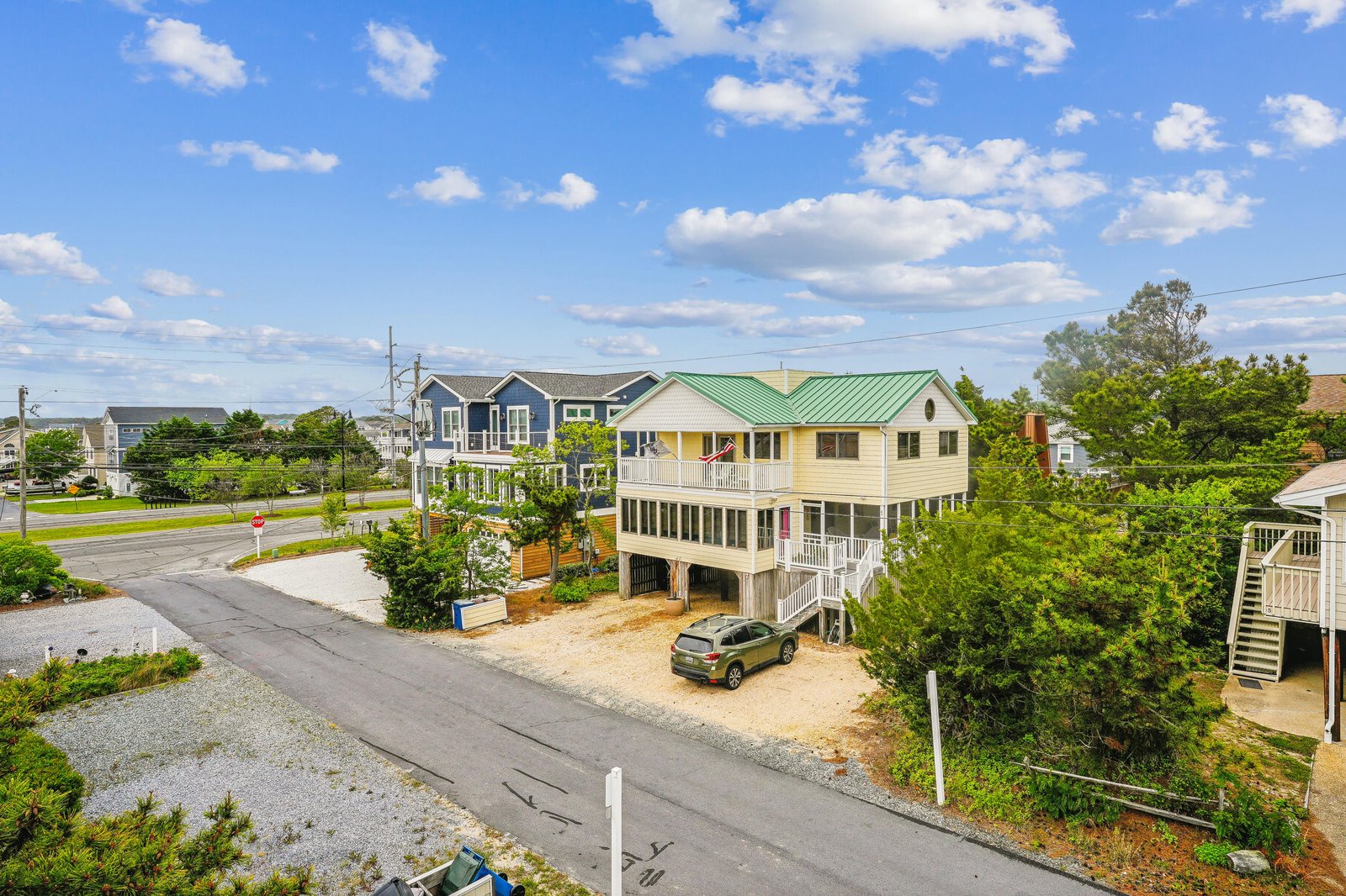 Aerial view of the property in a quiet coastal neighborhood, with dedicated parking and natural landscaping surrounding the beach house.