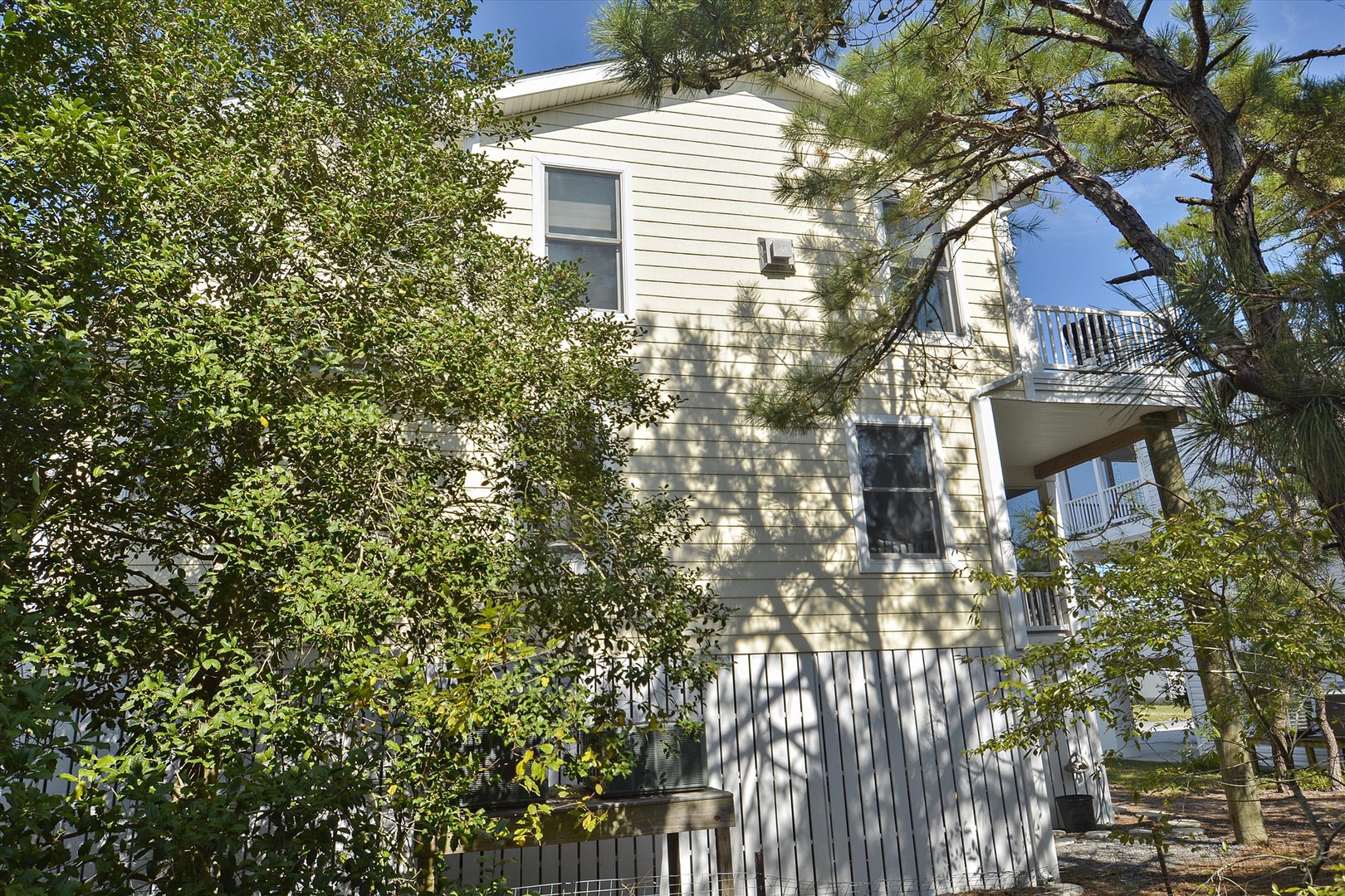 Light-colored multi-level vacation home nestled among mature trees and natural greenery, featuring multiple balconies and a peaceful wooded setting.