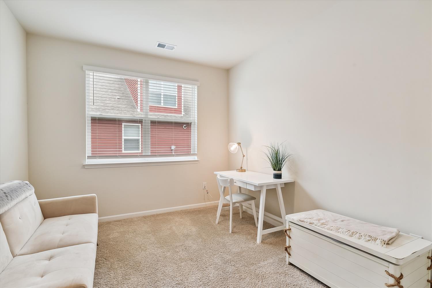 Your bright workspace awaits with a clean desk, comfy chair, and natural light streaming through windows overlooking the neighborhood.