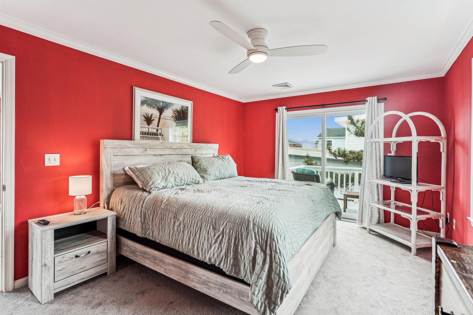 Your vibrant bedroom suite offers a comfy bed and balcony access with palm-lined coastal views, all kept cool by overhead fan.