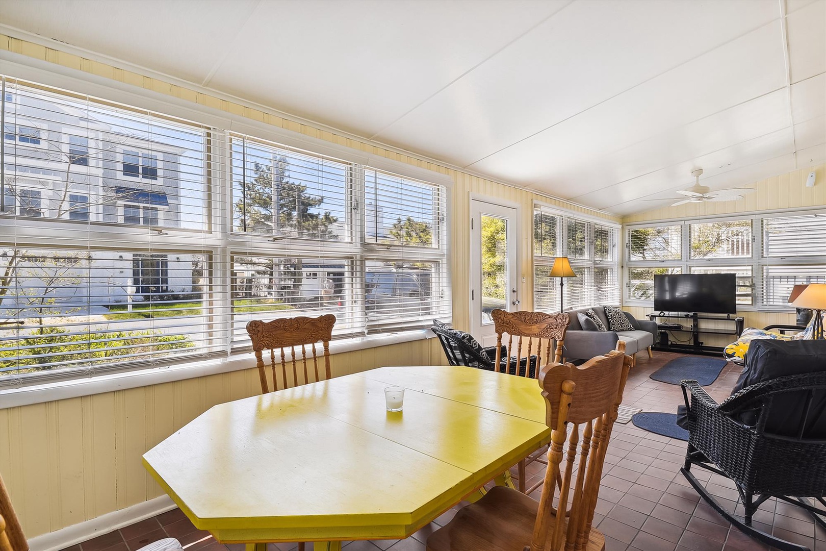 Relax in your bright, sun-filled living space where large windows frame peaceful neighborhood views. Unwind on the comfortable seating or gather around the cheerful yellow dining table for morning coffee or evening meals.