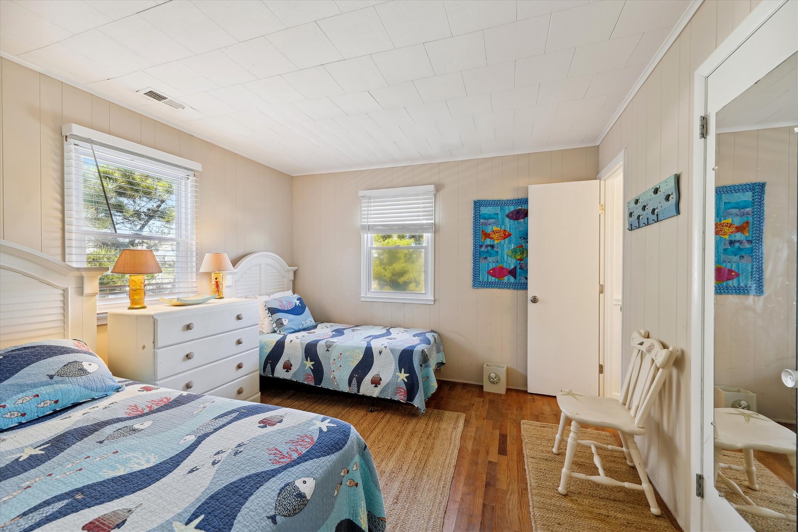Your kids will love this cheerful twin bedroom with its playful ocean-themed bedding and warm natural light streaming through double windows. A cozy retreat for restful nights by the shore.