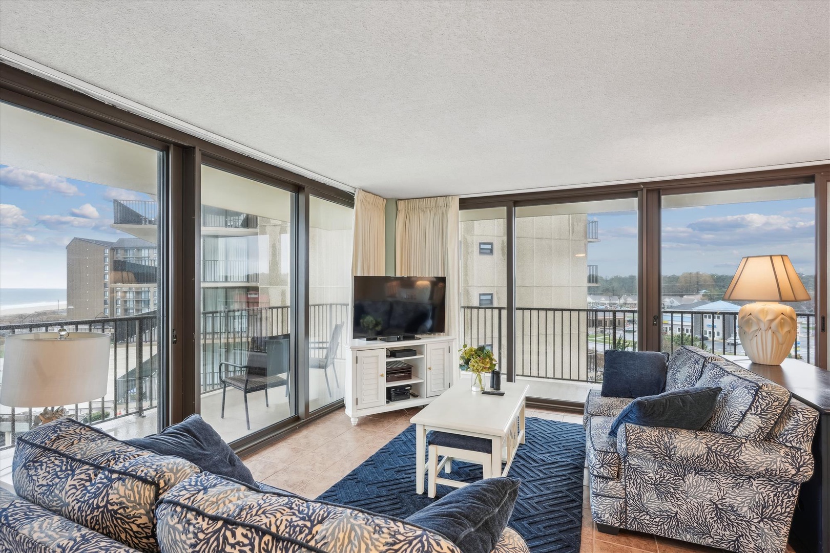 Relax in your bright living space with floor-to-ceiling windows showcasing stunning city views while you unwind on plush patterned seating.