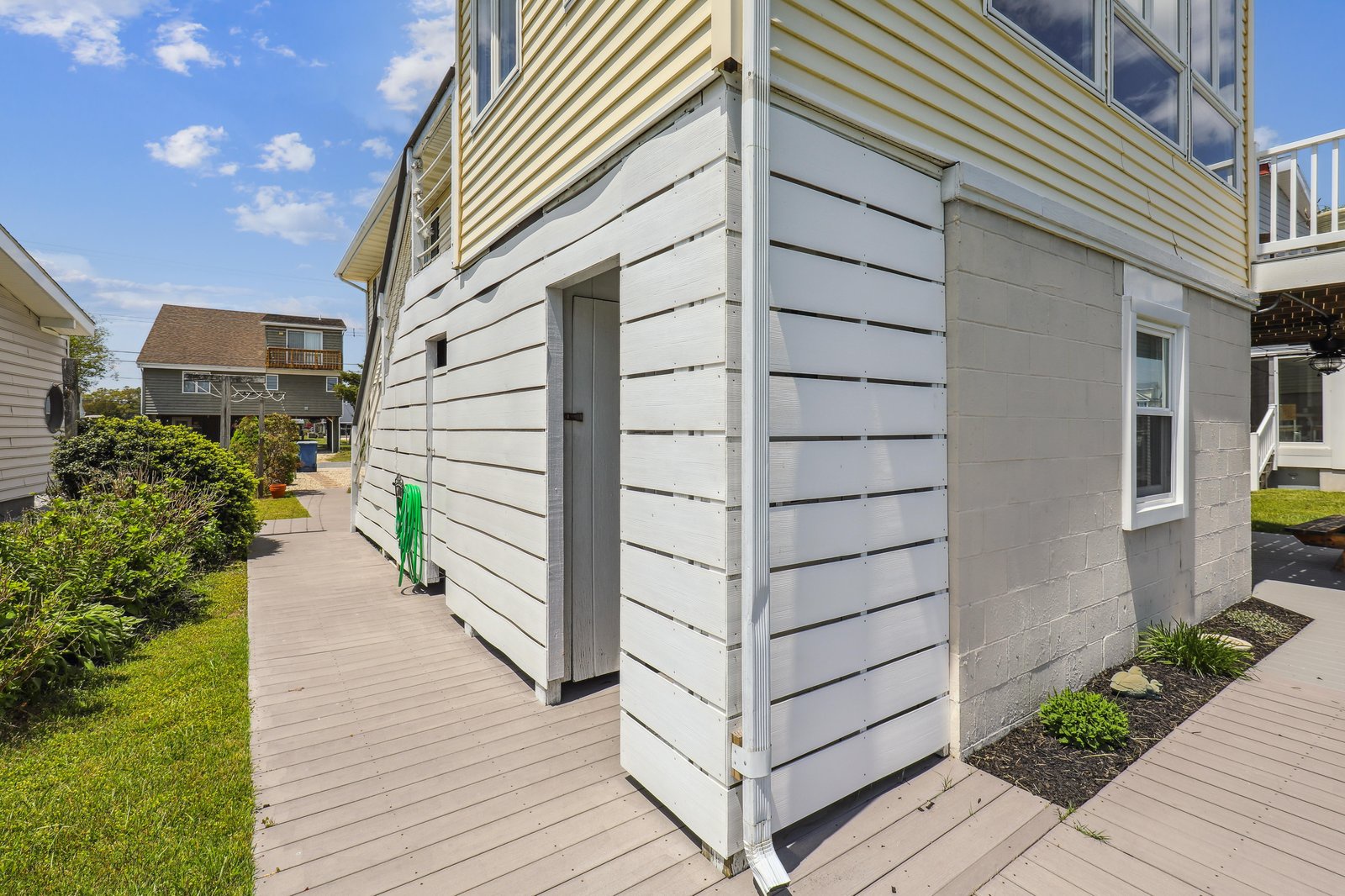 A charming coastal rental tucked into a sunny neighborhood, with beach homes lining the quiet street and a bright sky overhead—your relaxing getaway starts here.