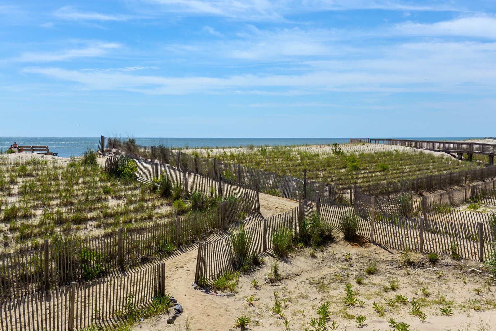 A scenic coastal destination featuring protected dunes with natural grasses and wooden boardwalk access leading to pristine sandy shores and ocean waters.