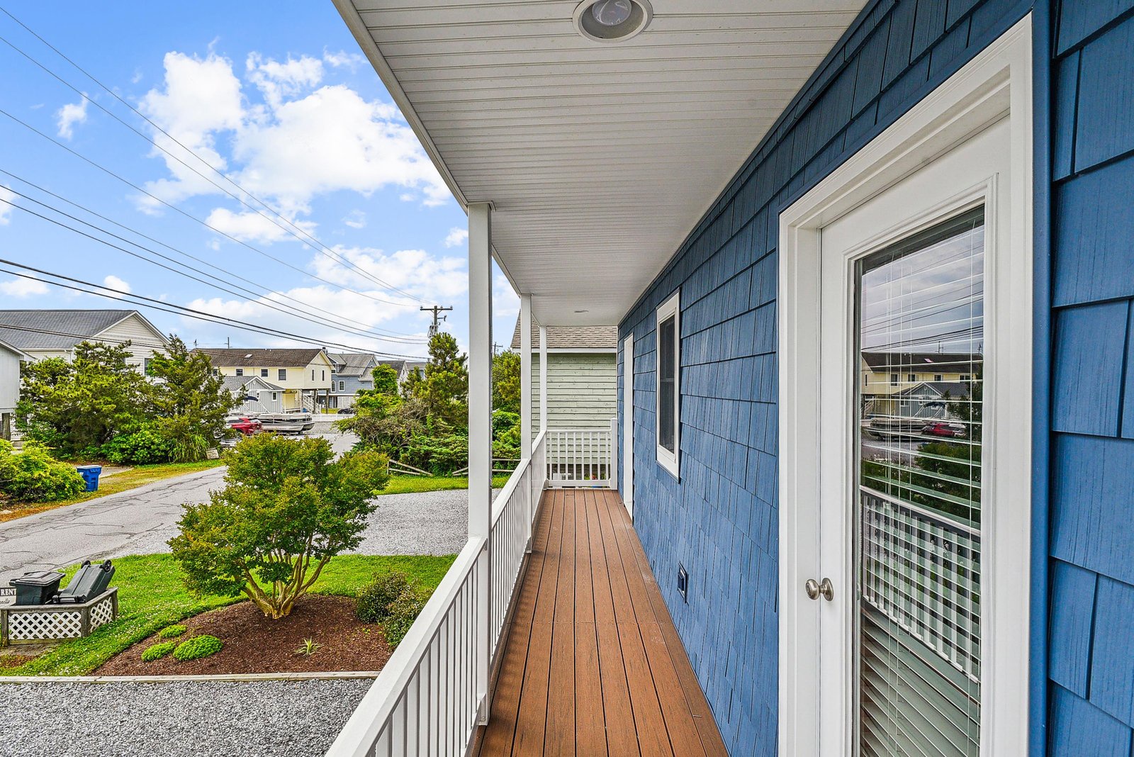 Charming blue exterior with a private covered balcony overlooking a peaceful residential neighborhood with green lawns and nearby homes.