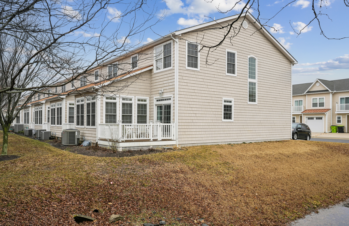 Charming beachside cottage with classic shingled exterior and spacious wraparound porch in peaceful residential neighborhood.