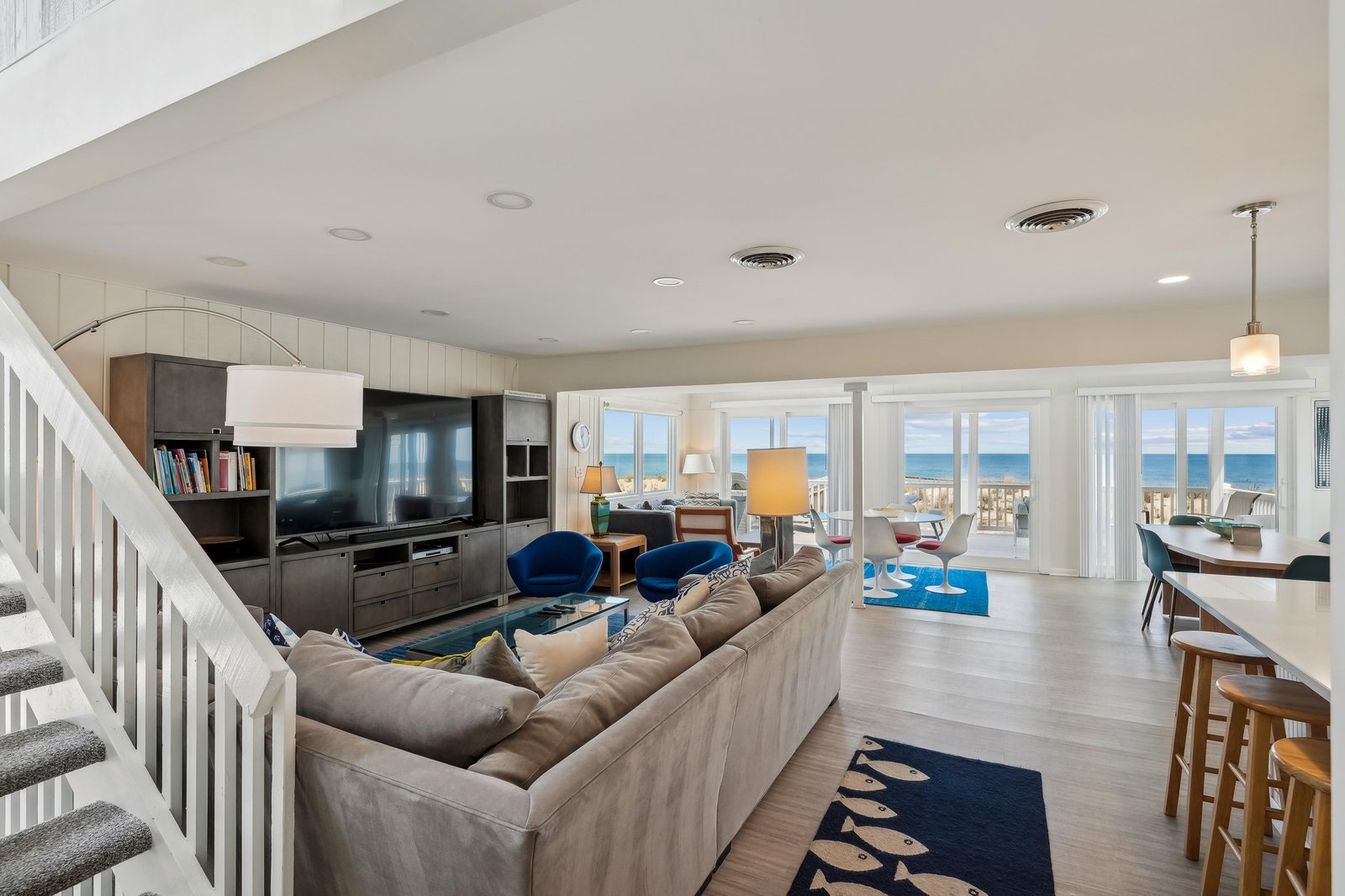 Spacious open-concept living area with panoramic ocean views through floor-to-ceiling windows. Relax on plush seating, gather at the kitchen bar, and step directly onto your private deck overlooking the water.