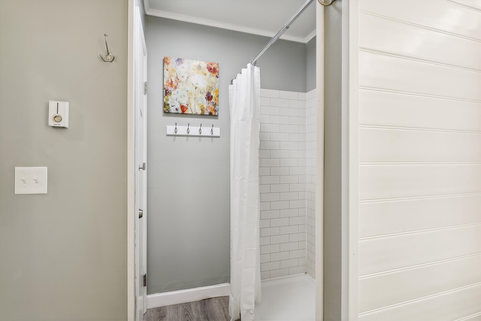Freshen up in your private subway-tiled shower with soft gray walls, floral artwork, and convenient hooks for towels and robes.