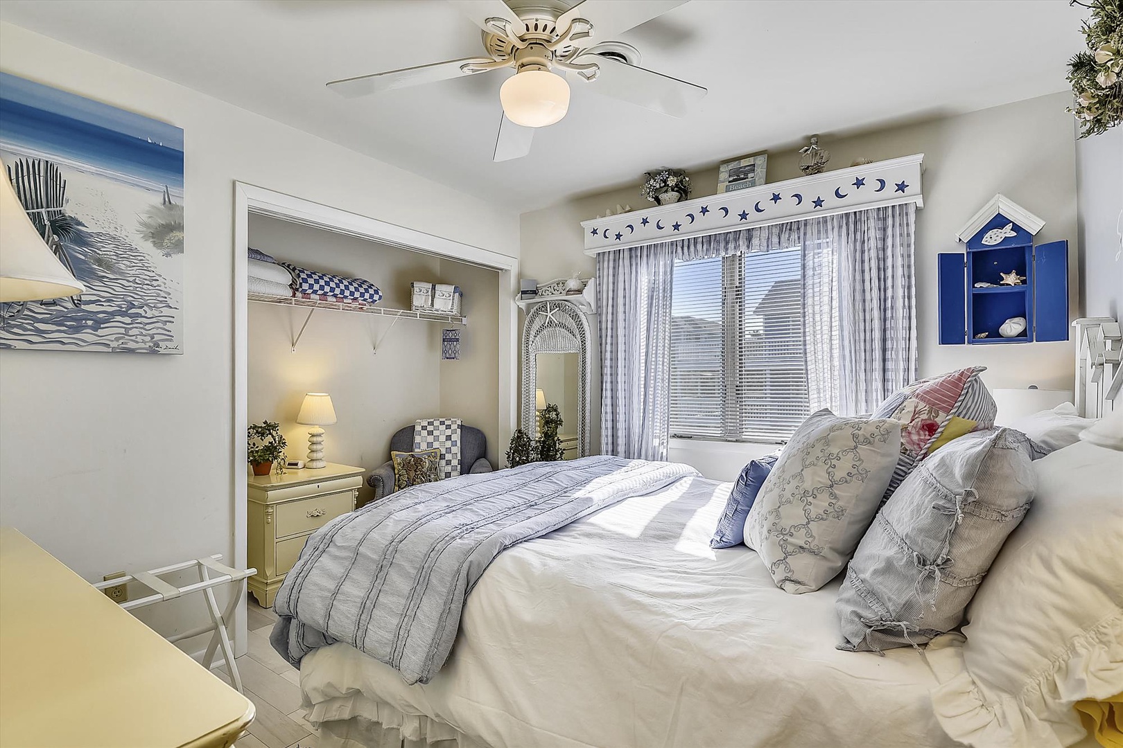 Sink into the plush bedding and feel the coastal charm surround you—beach-inspired décor, soft light from the ceiling fan, and a cozy nook invite pure relaxation.