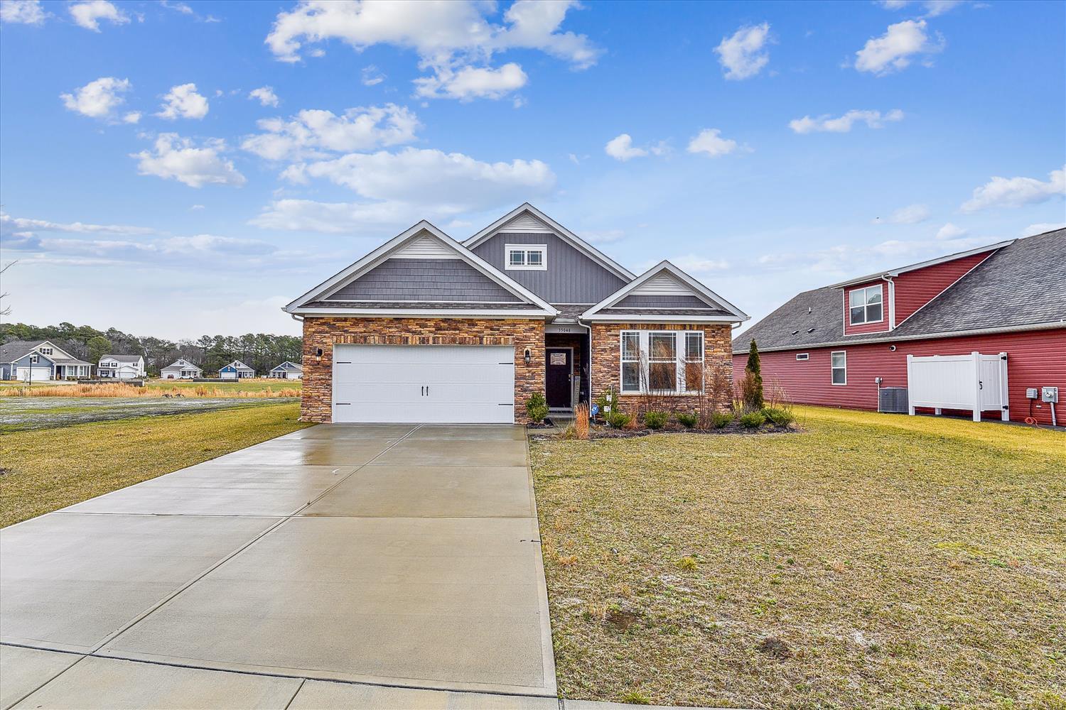 Single-family home in a residential neighborhood with attached two-car garage, stone and siding exterior, and spacious front lawn under open skies.