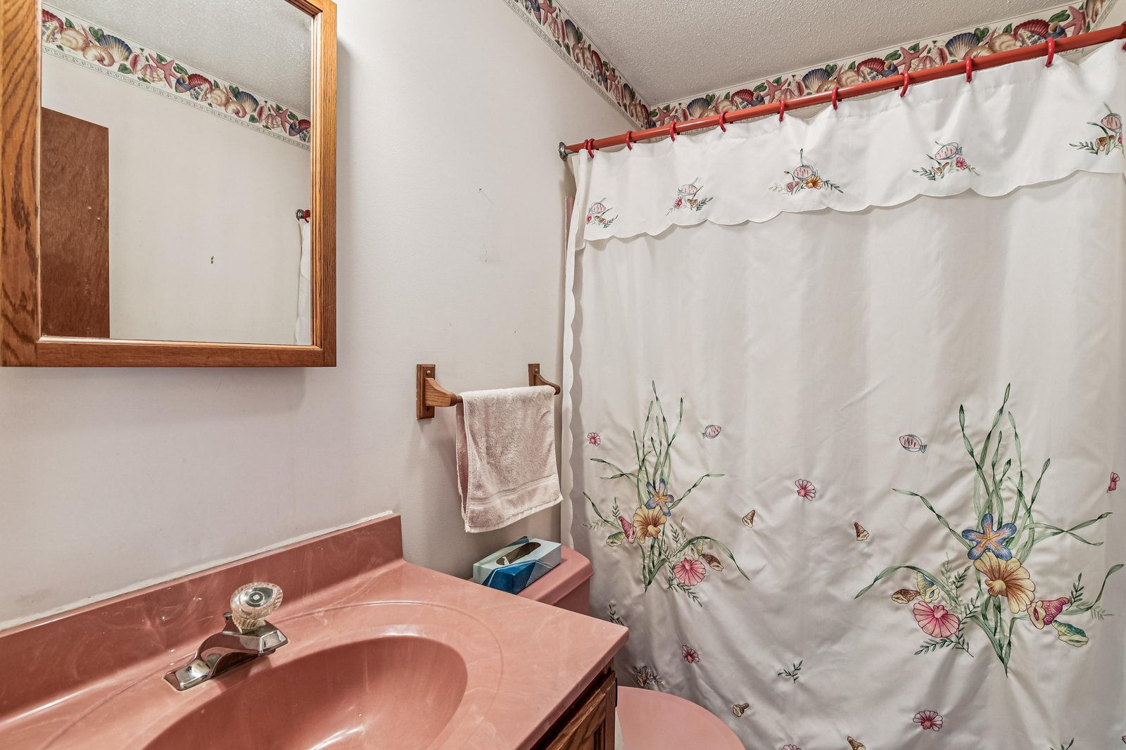 Vintage charm meets homey comfort in this cozy bathroom, with a floral curtain and warm pink fixtures inviting you to freshen up after a day of adventure.