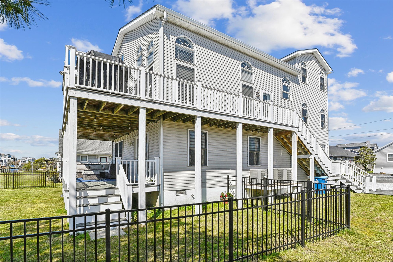 A spacious elevated coastal property with white siding and wraparound decks. The raised design features shaded ground-level areas, outdoor access stairs, and a fenced lawn—ideal for waterfront living.