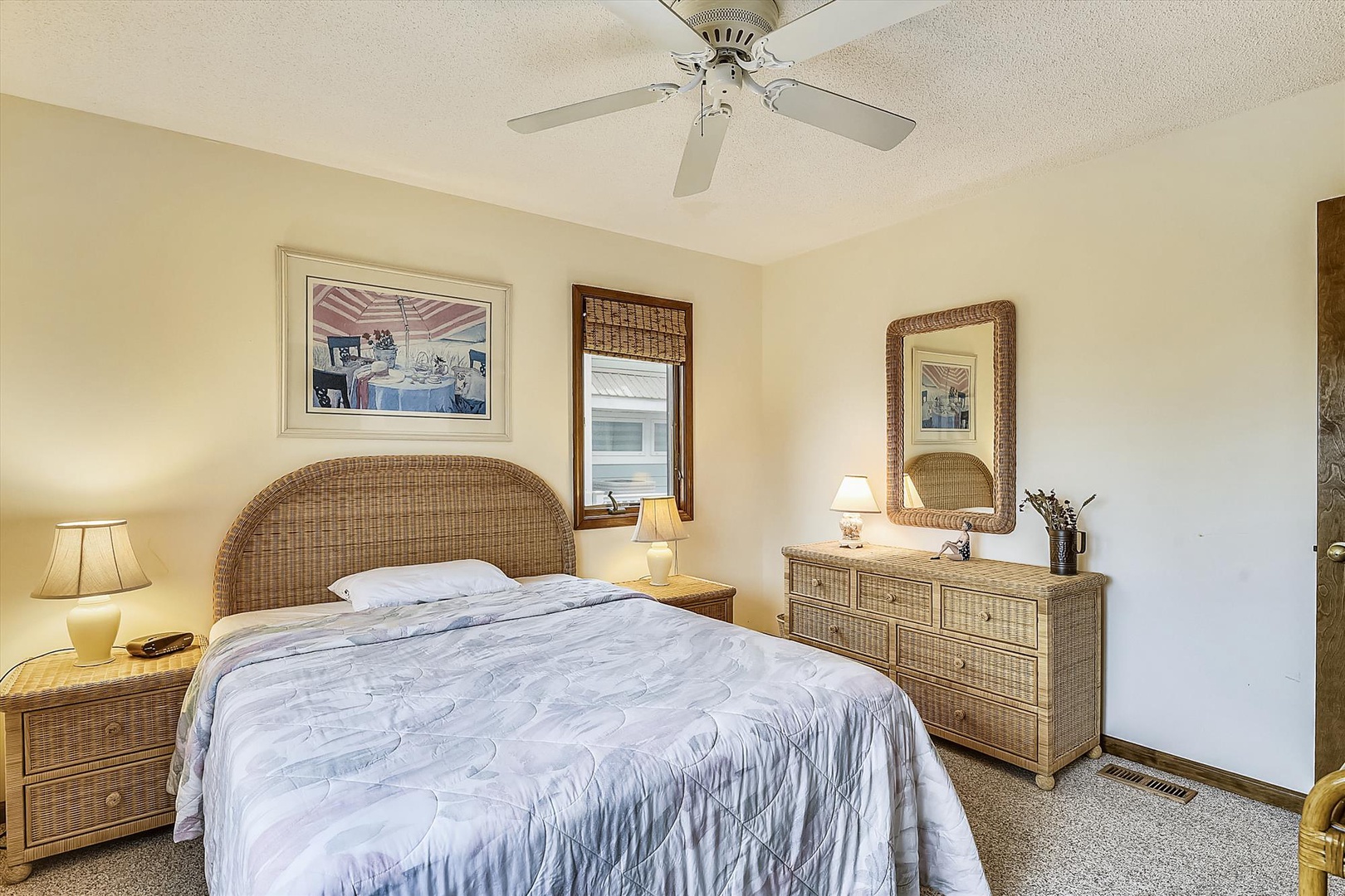 Drift off in your cozy bedroom with wicker furnishings, soft lighting, and a gentle ceiling fan for the perfect night's sleep.