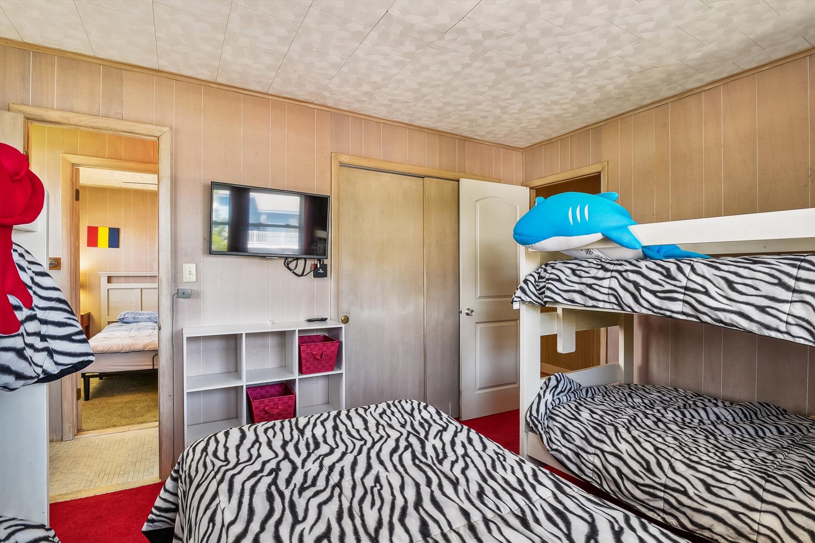Bright and playful bedroom with cozy bunk beds decked in zebra-striped linens, fun shark accents, and a TV for your entertainment. Adjacent bedroom offers extra sleeping space for your group.