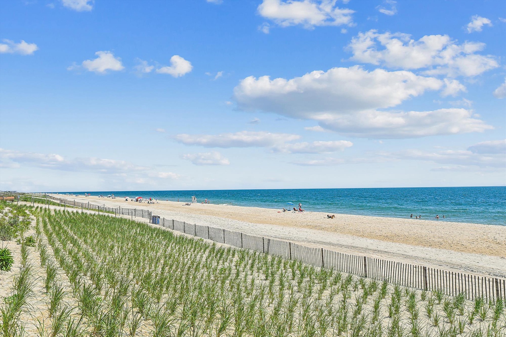 A pristine sandy beach stretches along the sparkling turquoise ocean, with gentle dunes and beach grass framing this beautiful coastal setting near the property.