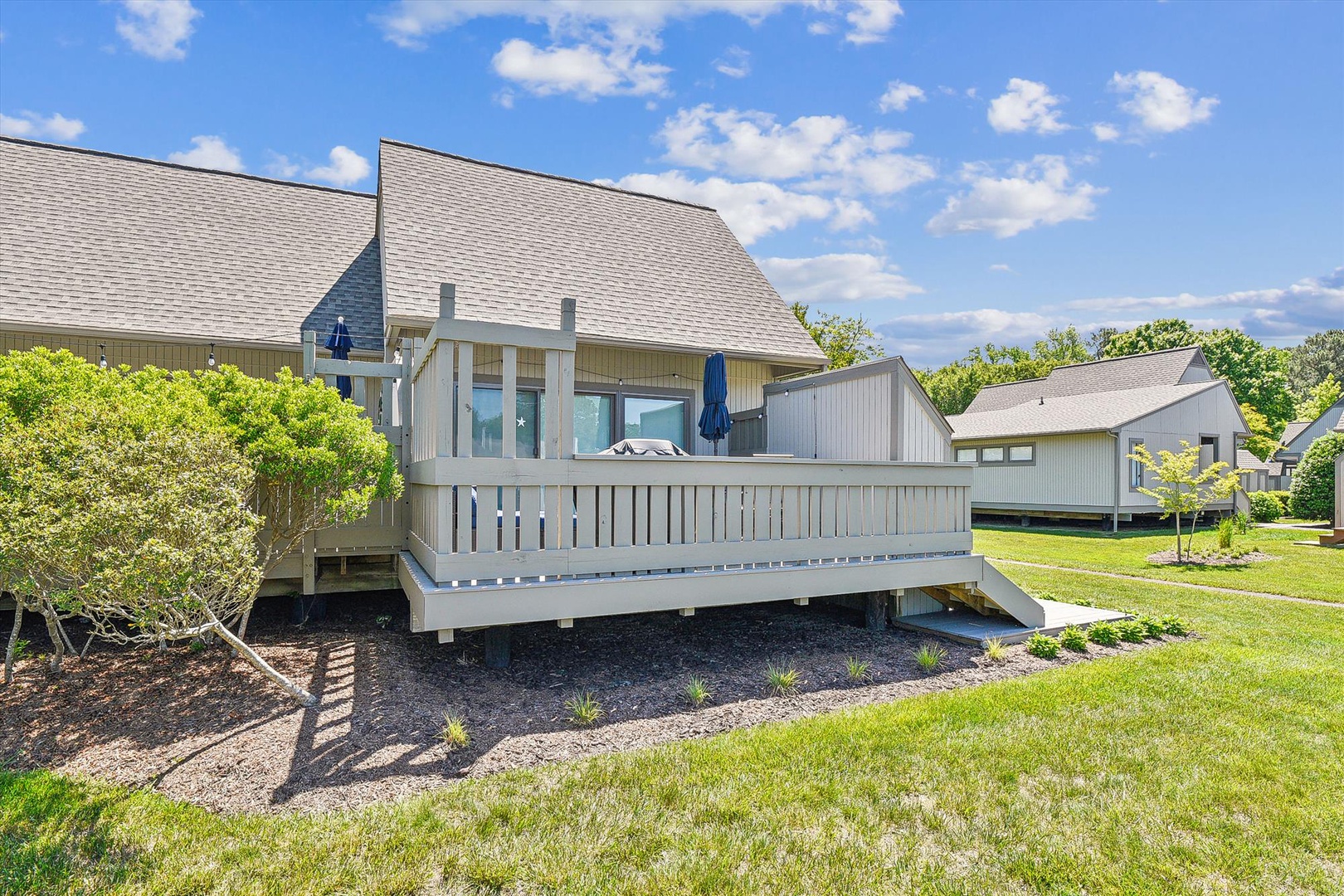 Spacious elevated deck with landscaped surroundings, featuring a covered outdoor seating area where you can relax and soak in the fresh air and blue skies.