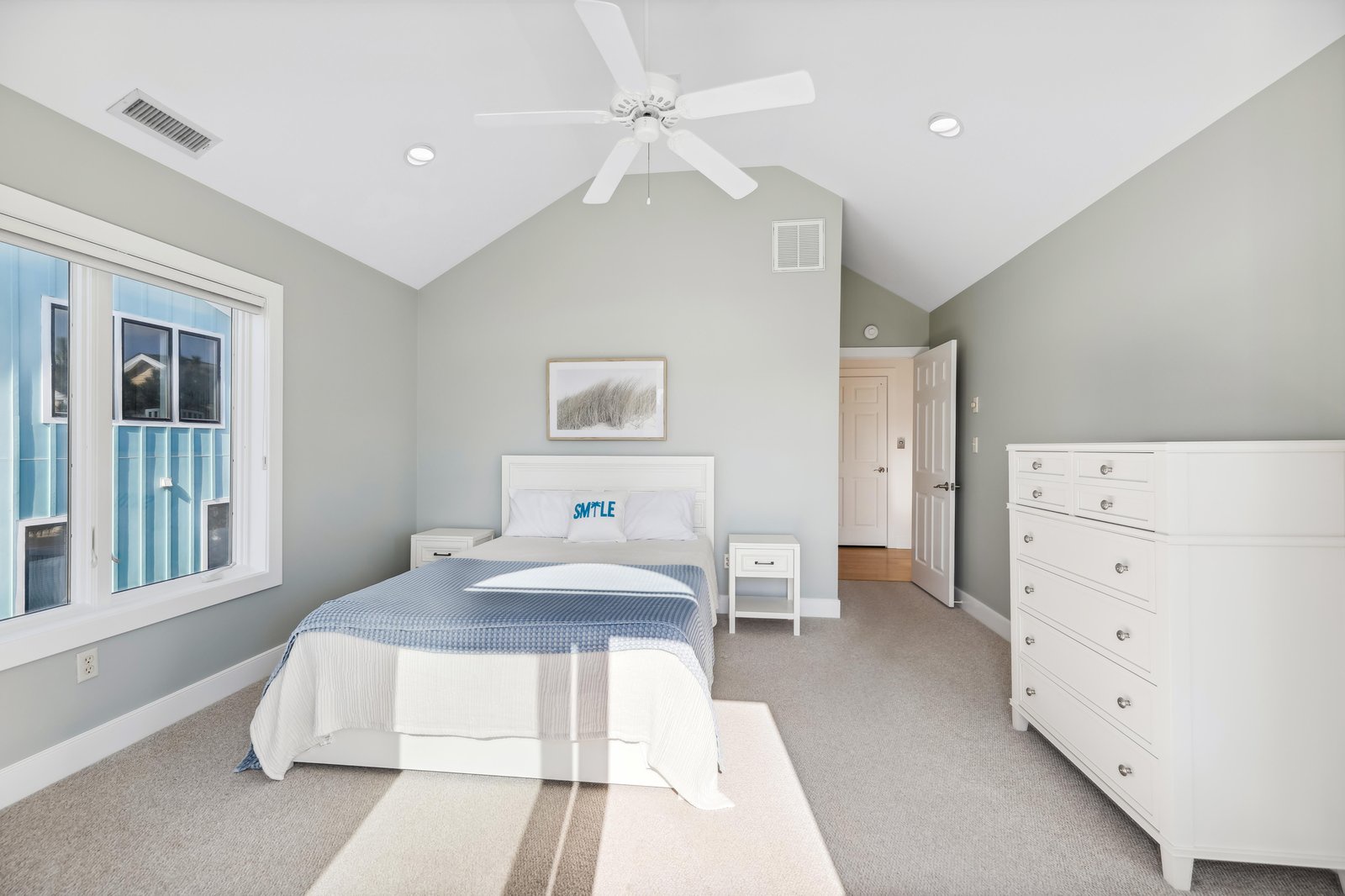Unwind in this airy bedroom with fresh coastal style, where vaulted ceilings, a soothing color palette, and a ceiling fan create your peaceful retreat after beach days.