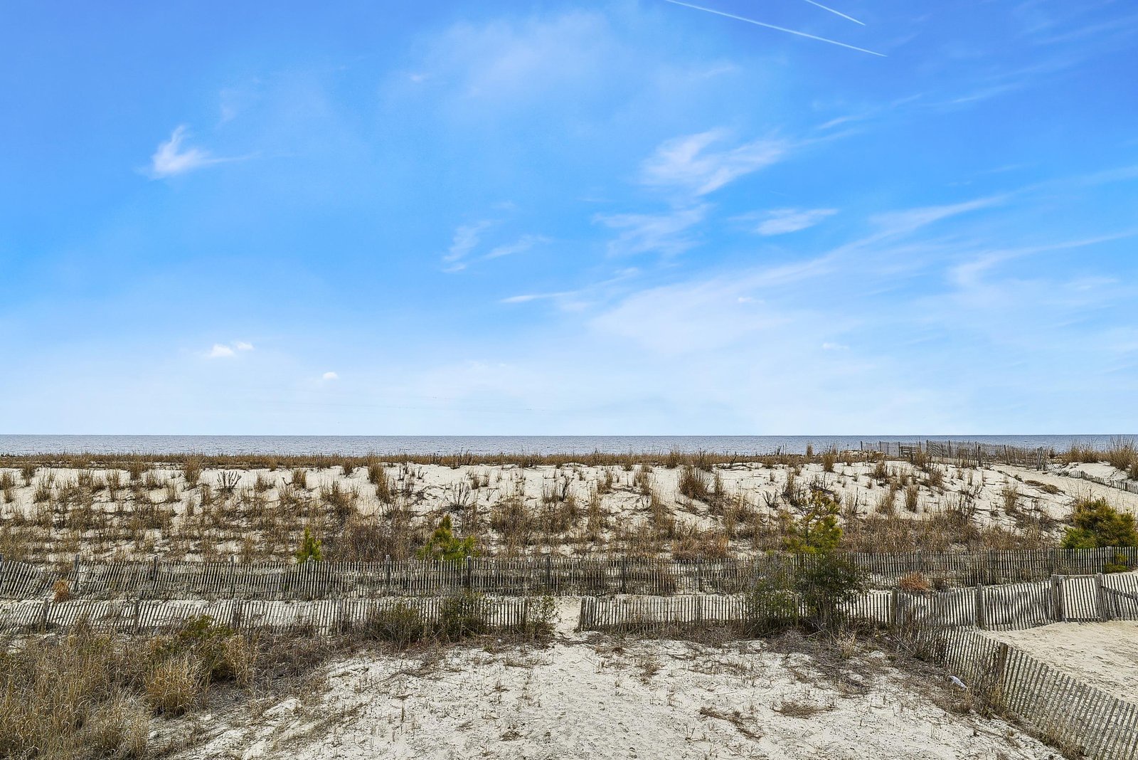 A protected dune landscape stretches toward the calm ocean under endless blue skies. This coastal setting offers direct access to quiet sandy beaches and refreshing sea breezes.