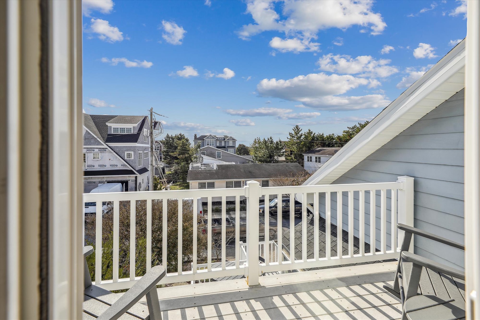 Private balcony overlooking a peaceful residential neighborhood, framed by coastal blue skies and surrounded by charming beach houses and greenery.