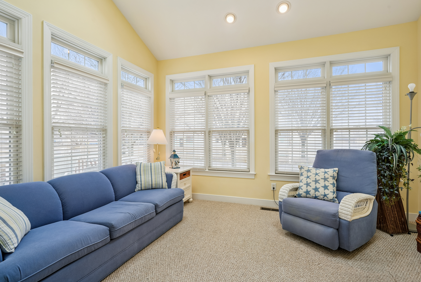 Sink into the plush blue sectional and armchair in your sun-drenched living room, where warm yellow walls and natural light create the perfect retreat.
