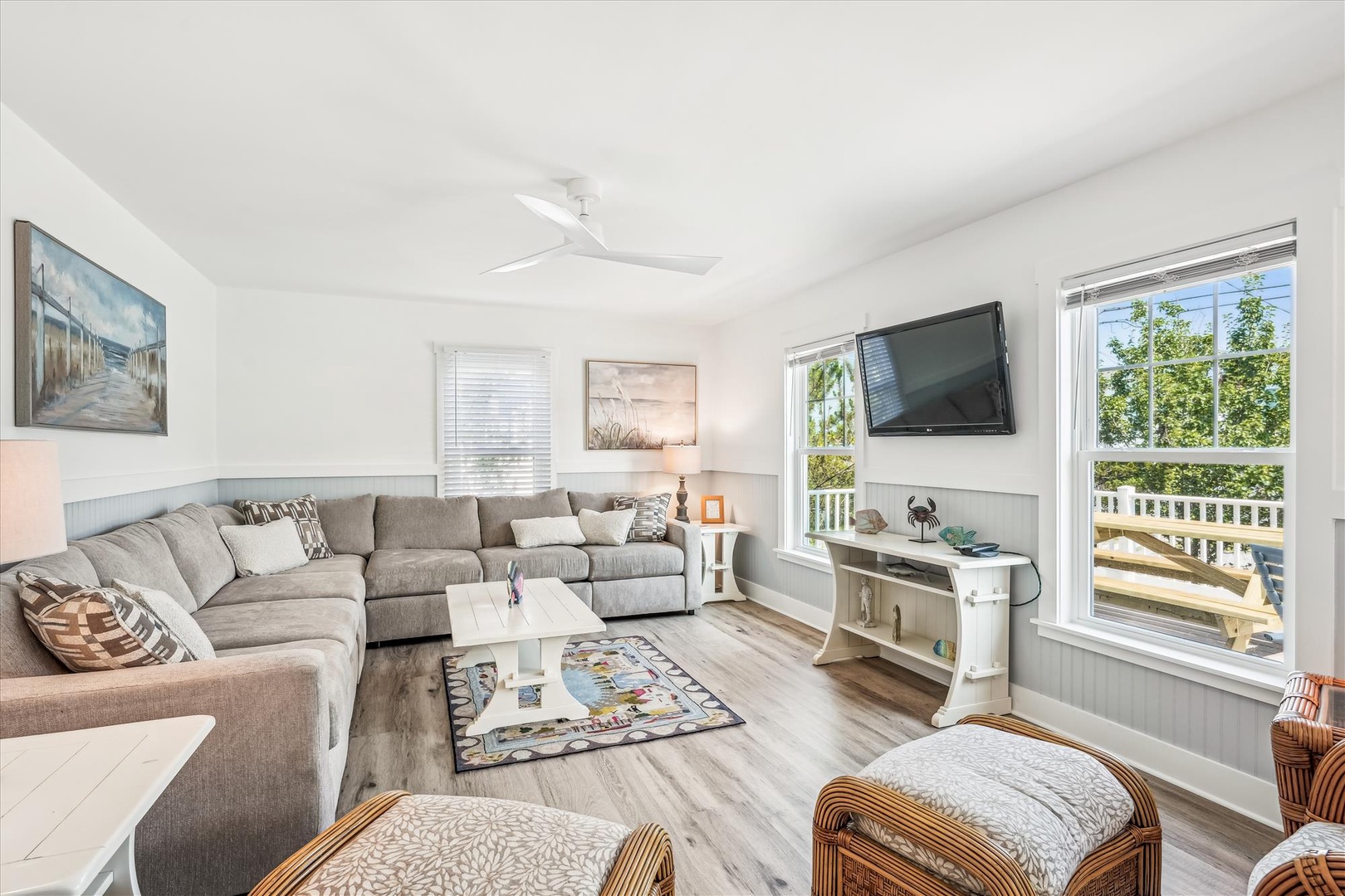 Relax in your spacious living room with sectional seating, wall-mounted TV, and peaceful garden views through bright windows.