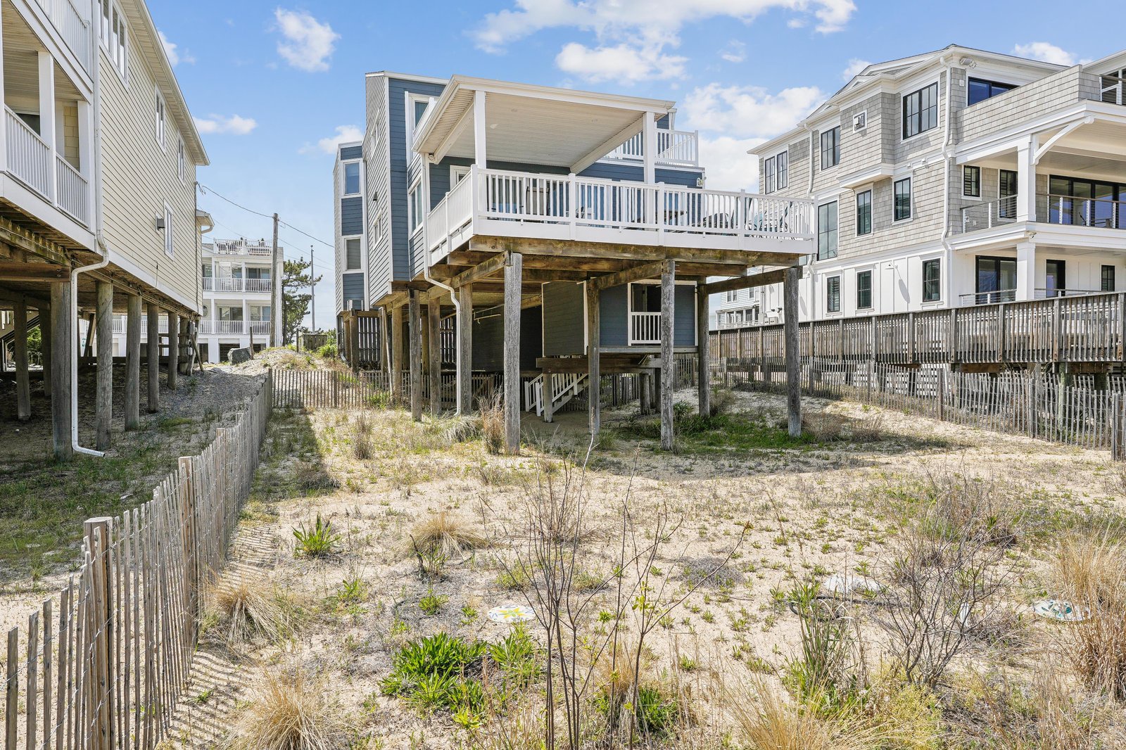 Elevated coastal home with covered deck and sandy pathway, located in a beachside neighborhood just steps from the shore.