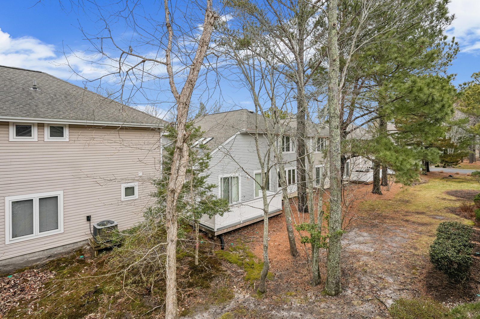 Elevated view of the property showcasing two multi-level structures nestled among mature trees in a peaceful residential setting with natural landscaping.