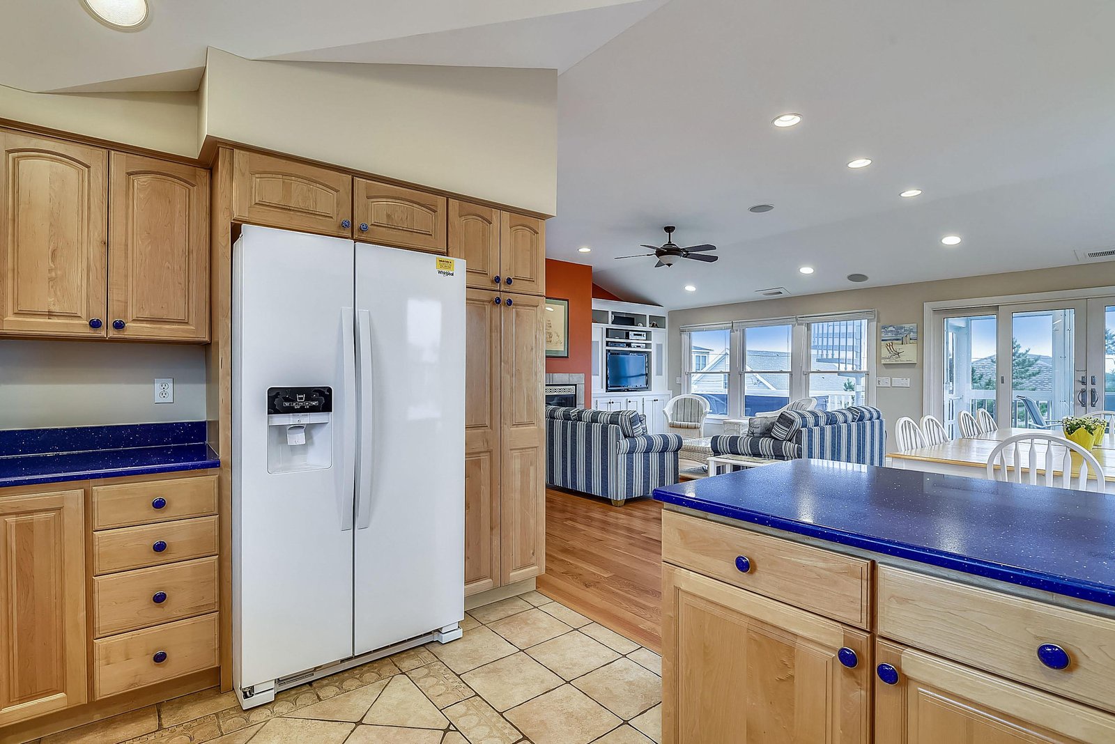 Bright, open-concept space with warm wood tones and vibrant blue accents. Fully equipped kitchen flows into cozy living and dining areas, all bathed in natural light from expansive windows.