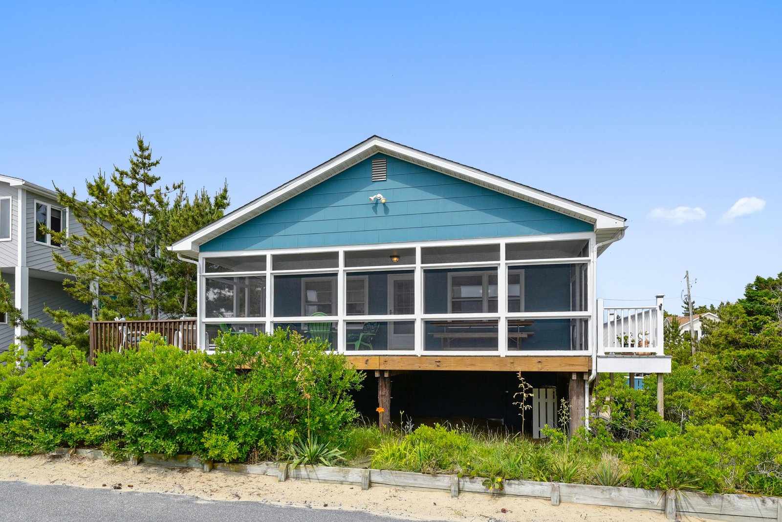 A charming coastal cottage nestled among dunes and greenery, offering a peaceful beachside retreat with sweeping ocean views just beyond the sand.